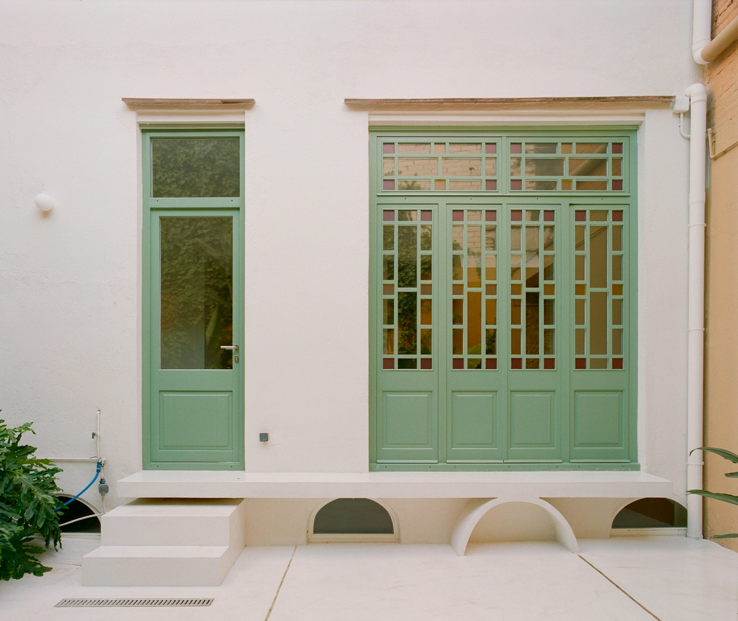 LL731 by Aramé Studio — A rendered facade with two green-painted timber-framed windows positioned asymmetrically on a white wall.