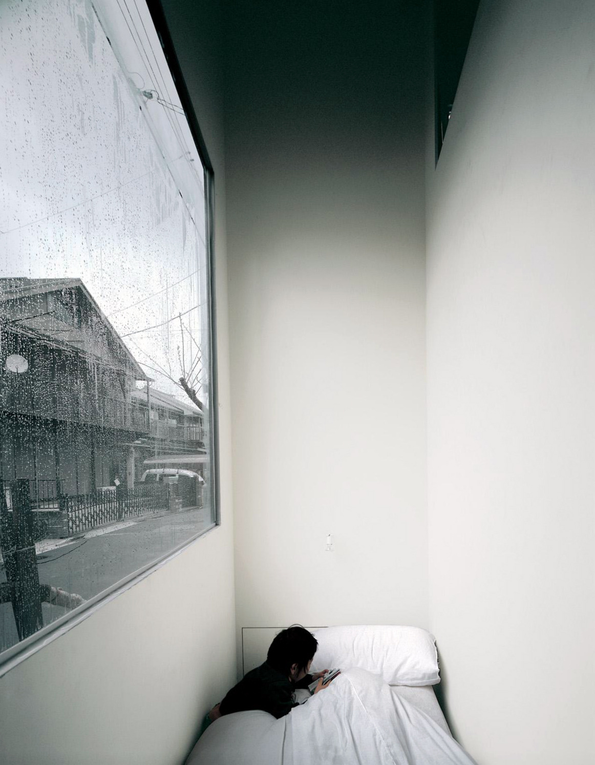 House in a Plum Grove by Kazuyo Sejima by Kazuyo Sejima & Associates — A narrow bedroom occupies the compressed interior of Sejima's vertical intervention, with a single bed positioned directly beneath a horizontal window that...