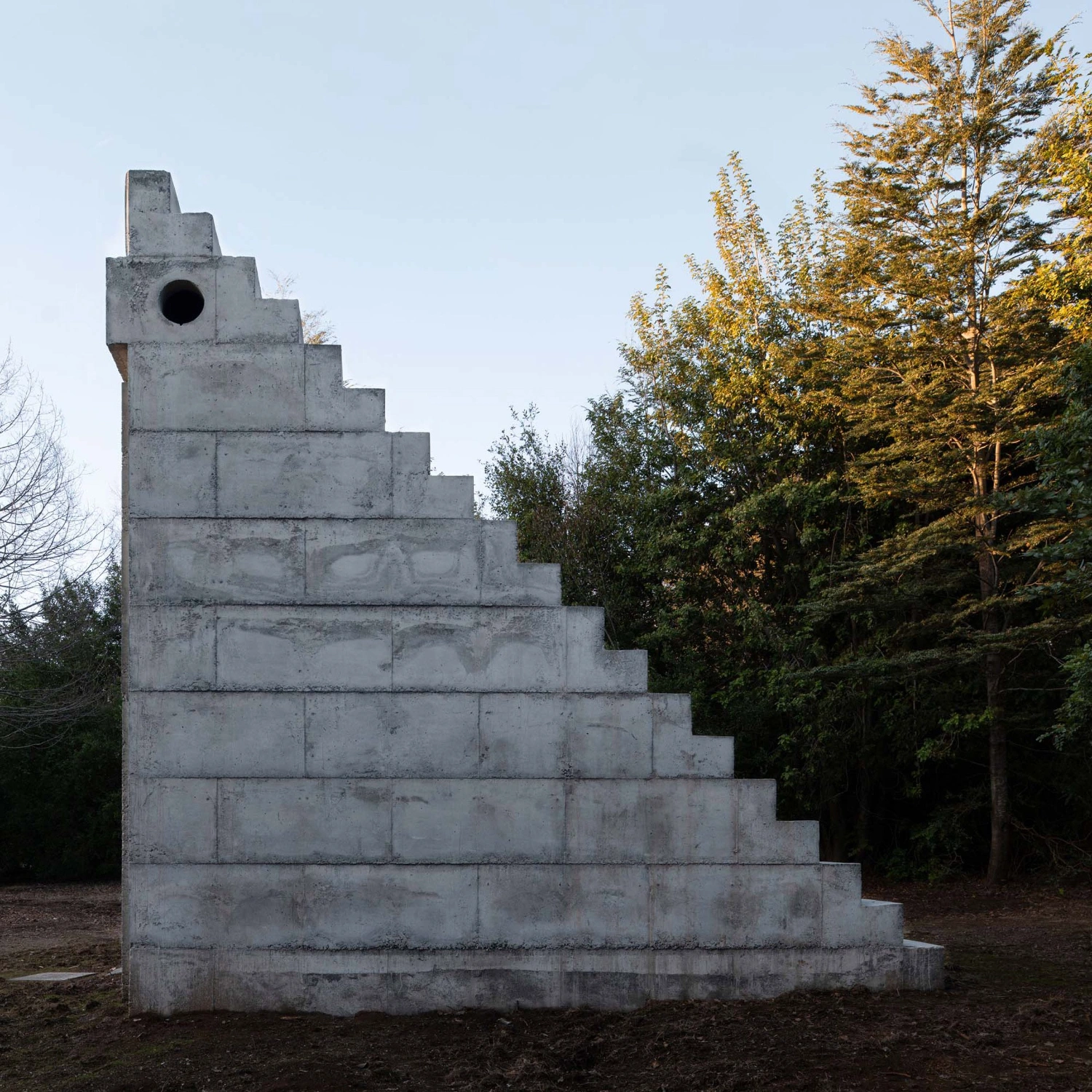 MIEL Pavilion by Pezo von Ellrichshausen — The MIEL Pavilion is photographed from the exterior, presenting its monolithic concrete form against a backdrop of golden-hour forest light.