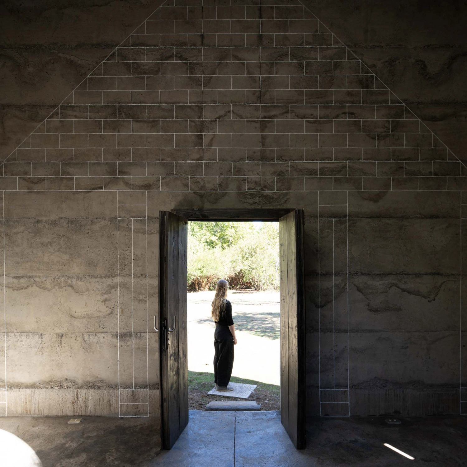 MIEL Pavilion by Pezo von Ellrichshausen — A figure stands silhouetted in the threshold of the MIEL Pavilion, framed by the dark timber doorway.