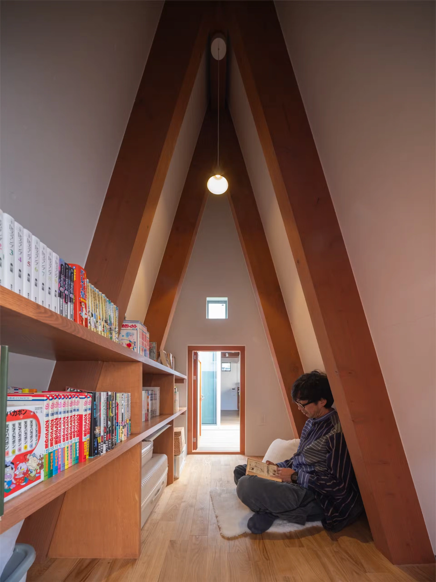 Little Village by Takeshi Hosaka — A child reads within a timber-lined alcove framed by two substantial angled wooden beams that form an inverted V.