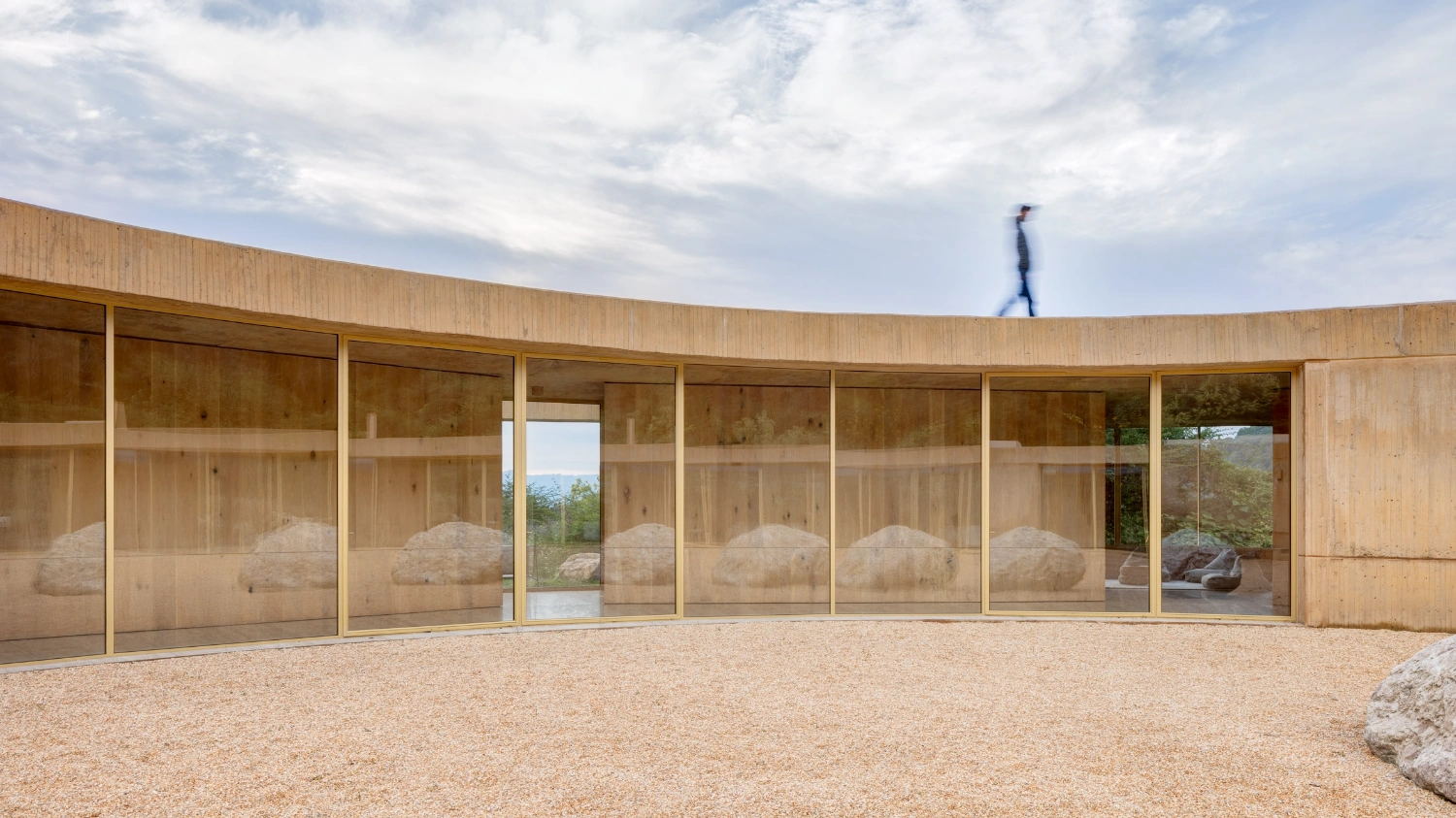 House 720 Degrees by Fernanda Canales Architecture — The curved timber-clad facade wraps continuously around the gravel courtyard, its warm ochre wood grain reflecting the earth palette of Valle de Bravo.