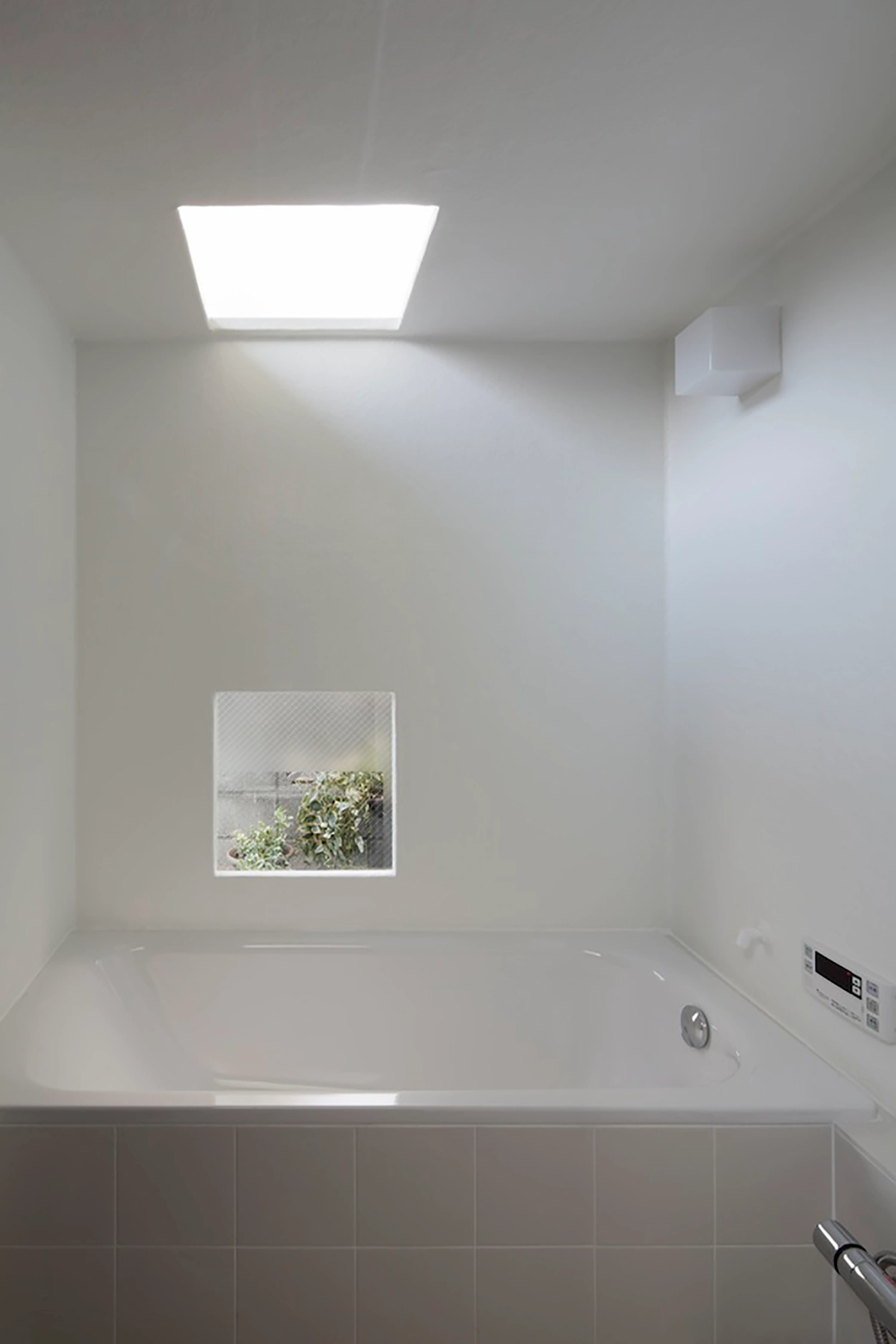 Tunnel House by Makiko Tsukada Architects — A bathroom interior flooded with diffuse light from a large rectangular skylight above, casting even illumination across white plaster walls.