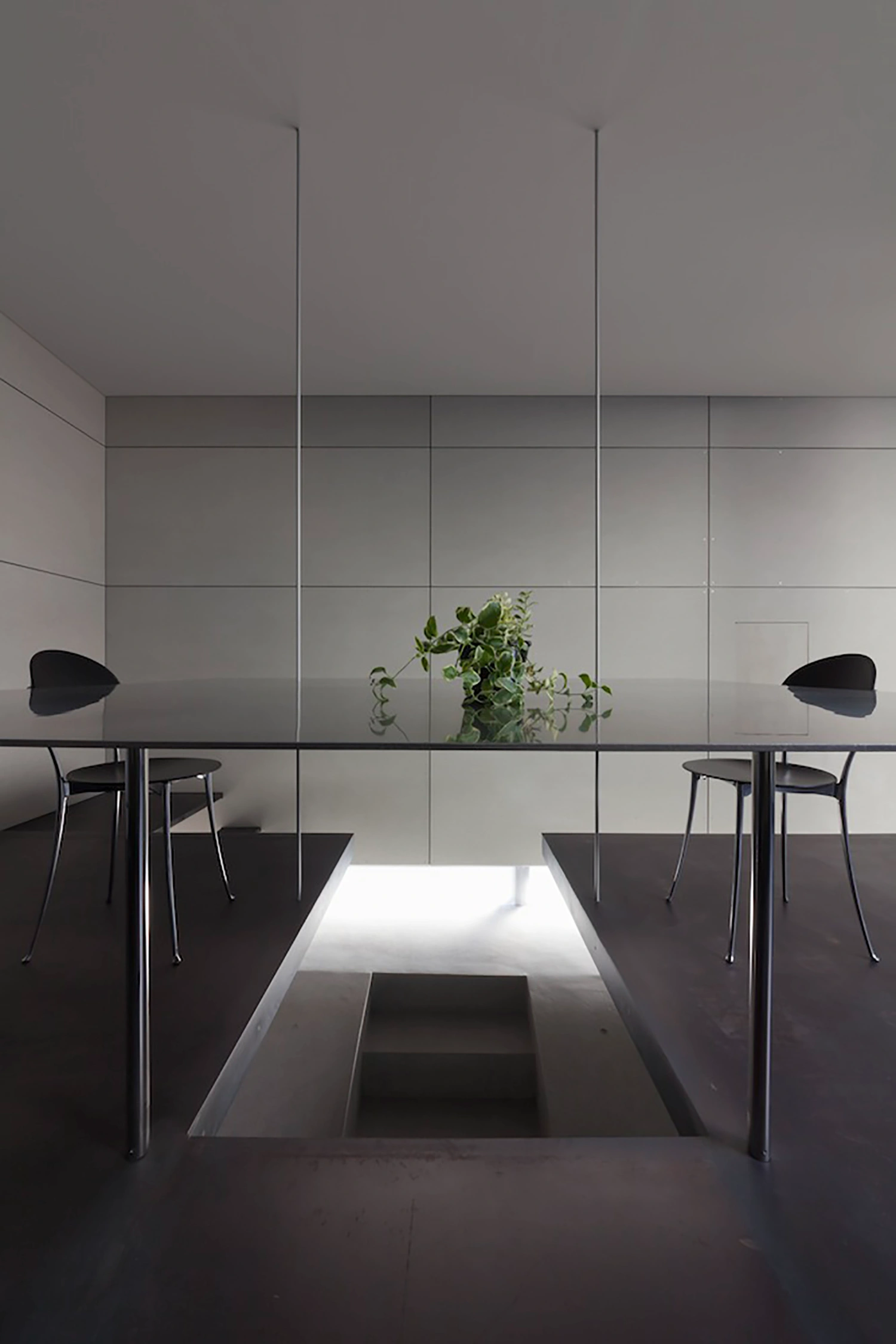 Tunnel House by Makiko Tsukada Architects — A symmetrical interior view of the Tunnel House reveals the architectural strategy at its core: two black metal-frame tables with curved-back chairs...