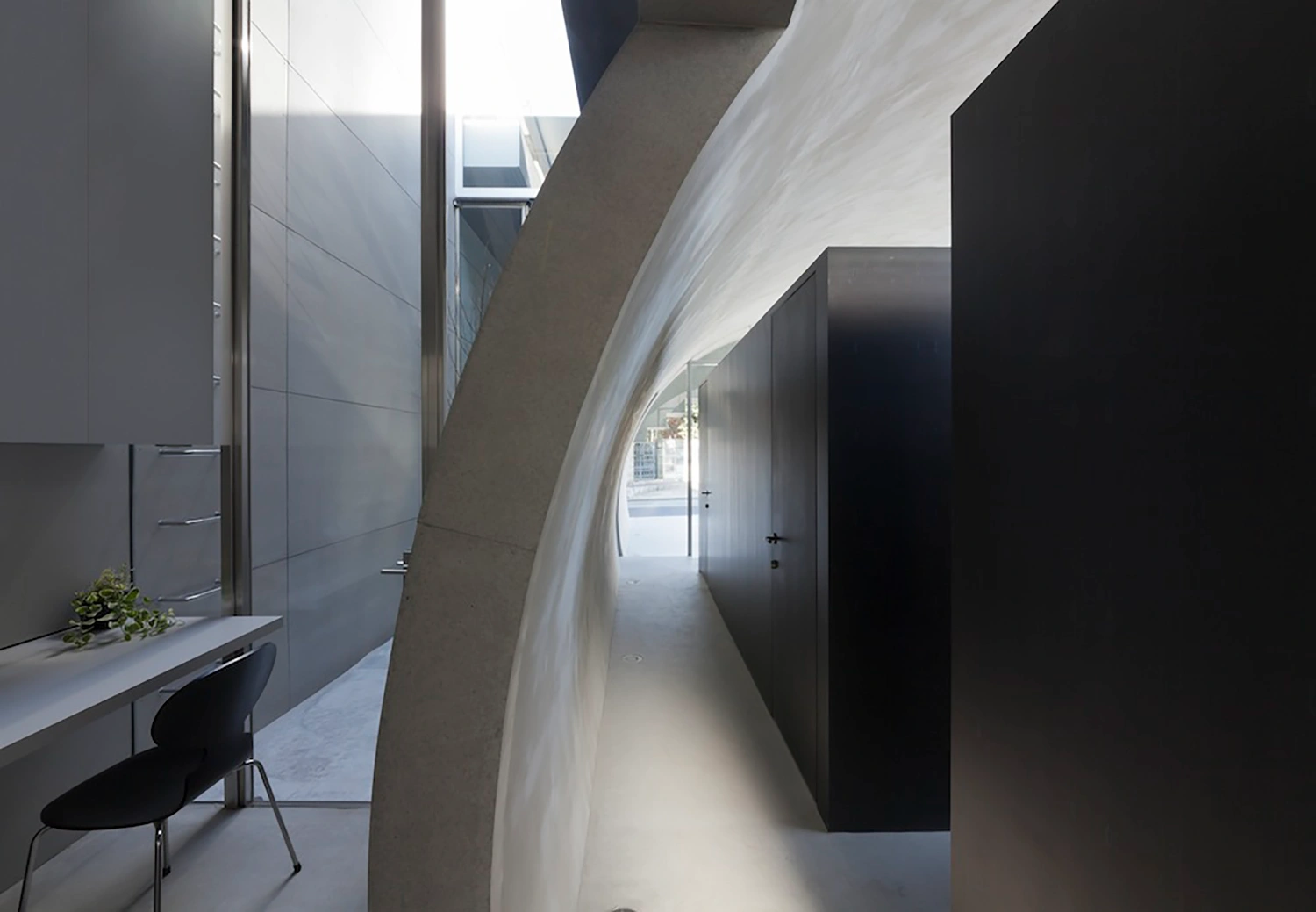 Tunnel House by Makiko Tsukada Architects — A narrow passage frames the project's defining architectural gesture: a quarter-cylinder void carved through the building's mass, its curved white concrete...