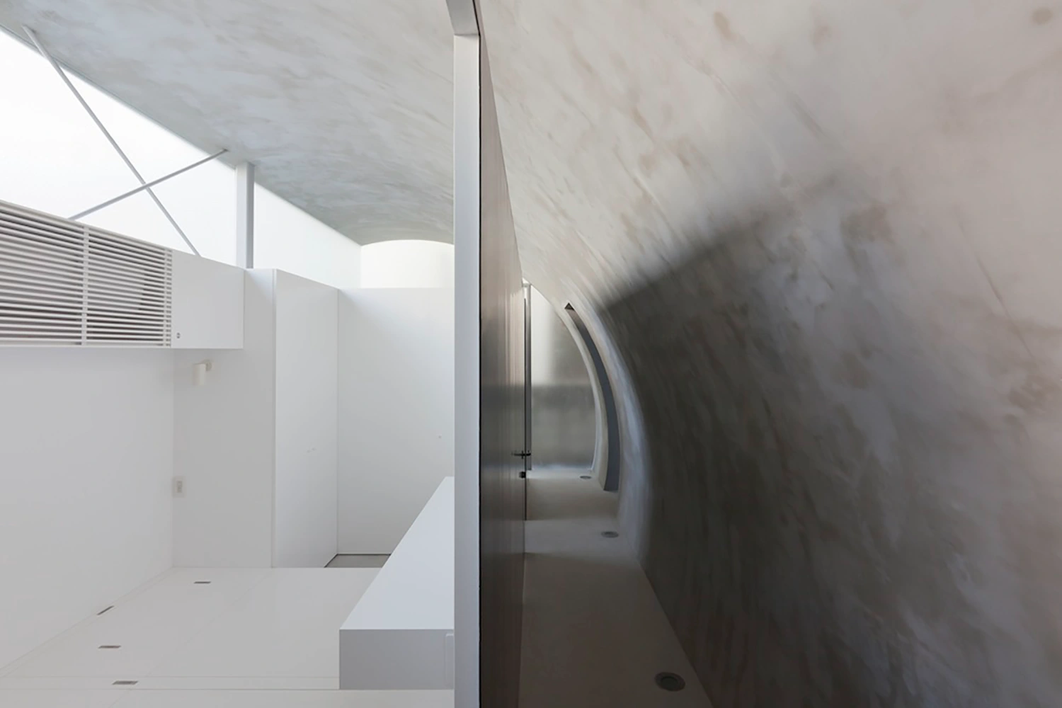 Tunnel House by Makiko Tsukada Architects — A view through the threshold of the quarter-cylinder void, where curved white concrete walls create a luminous tunnel receding into the interior.