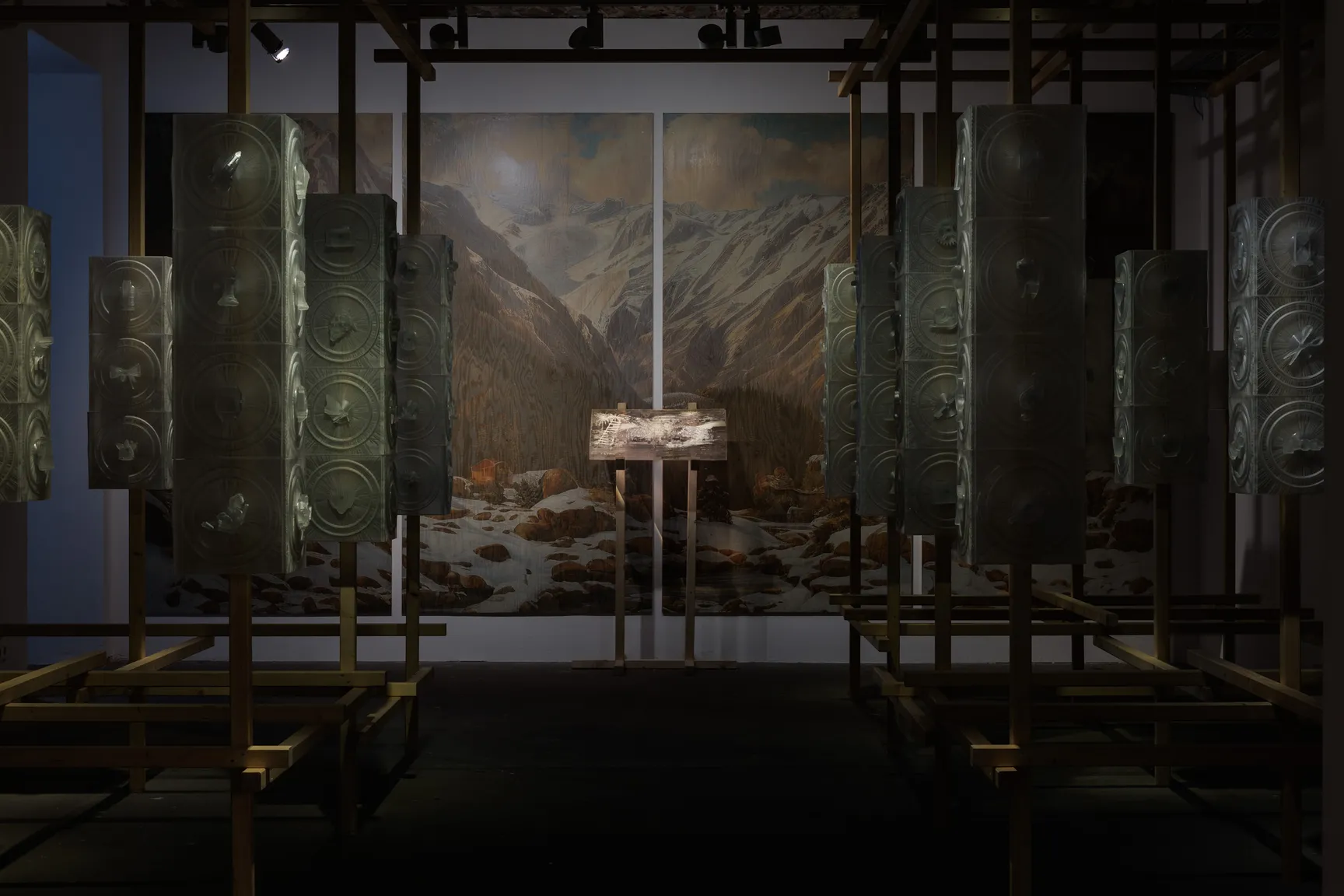 Starmirror by Holly Herndon & Mat Dryhurst at KW Institute for Contemporary Art — The exhibition interior frames a monumental wooden lattice tower at center, flanked by symmetrical rows of patinated bronze panels with embossed circular...