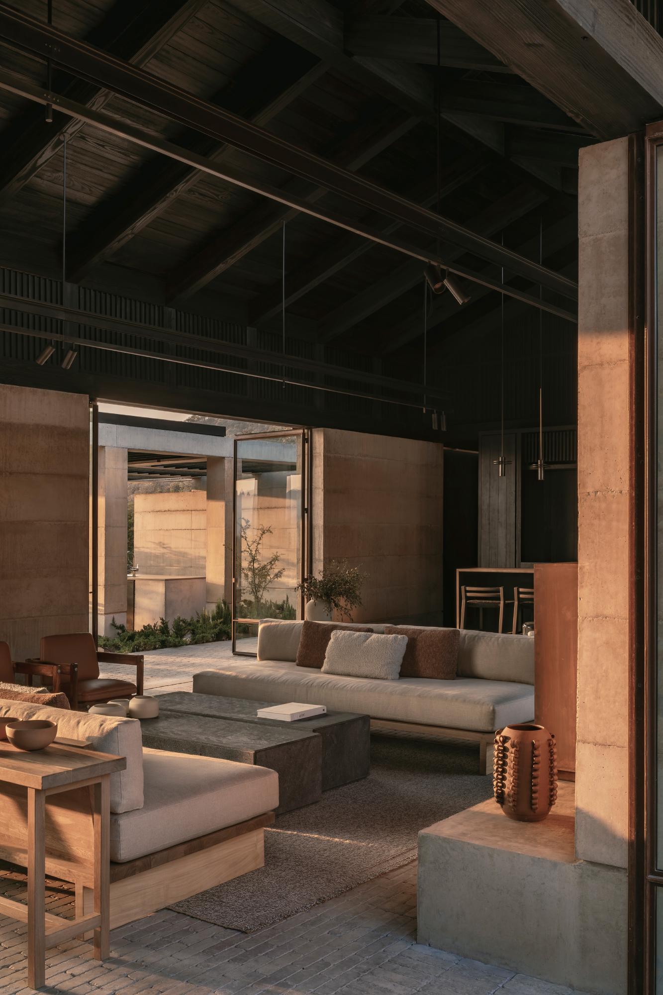 Casa el Espino by Soler Orozco Arquitectos — Interior living space bathed in golden-hour light, revealing the spatial relationship between the terracotta brick walls and timber-framed ceiling structure.