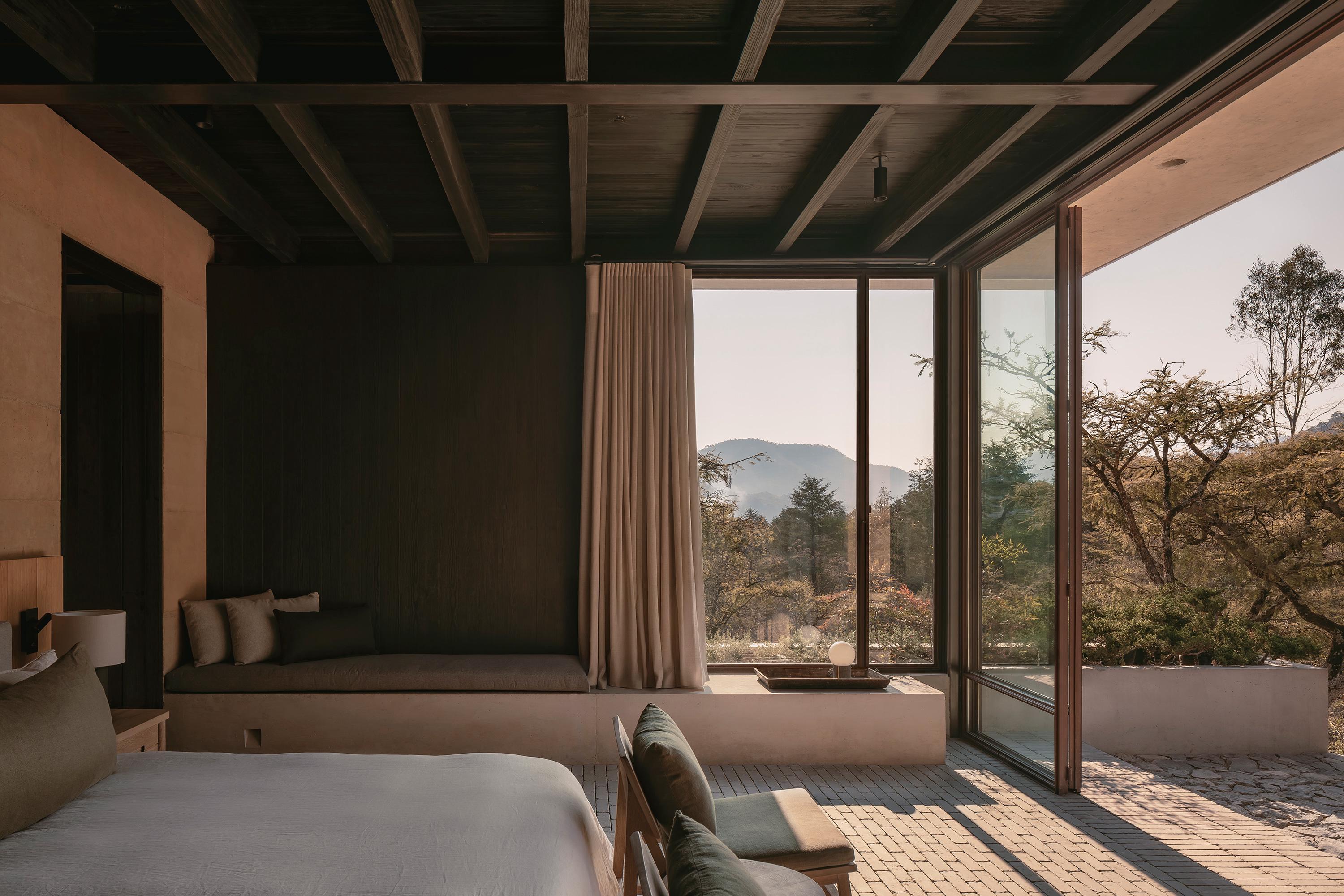 Casa el Espino by Soler Orozco Arquitectos — A bedroom interior facing expansive glazed doors that frame mountain landscape beyond.