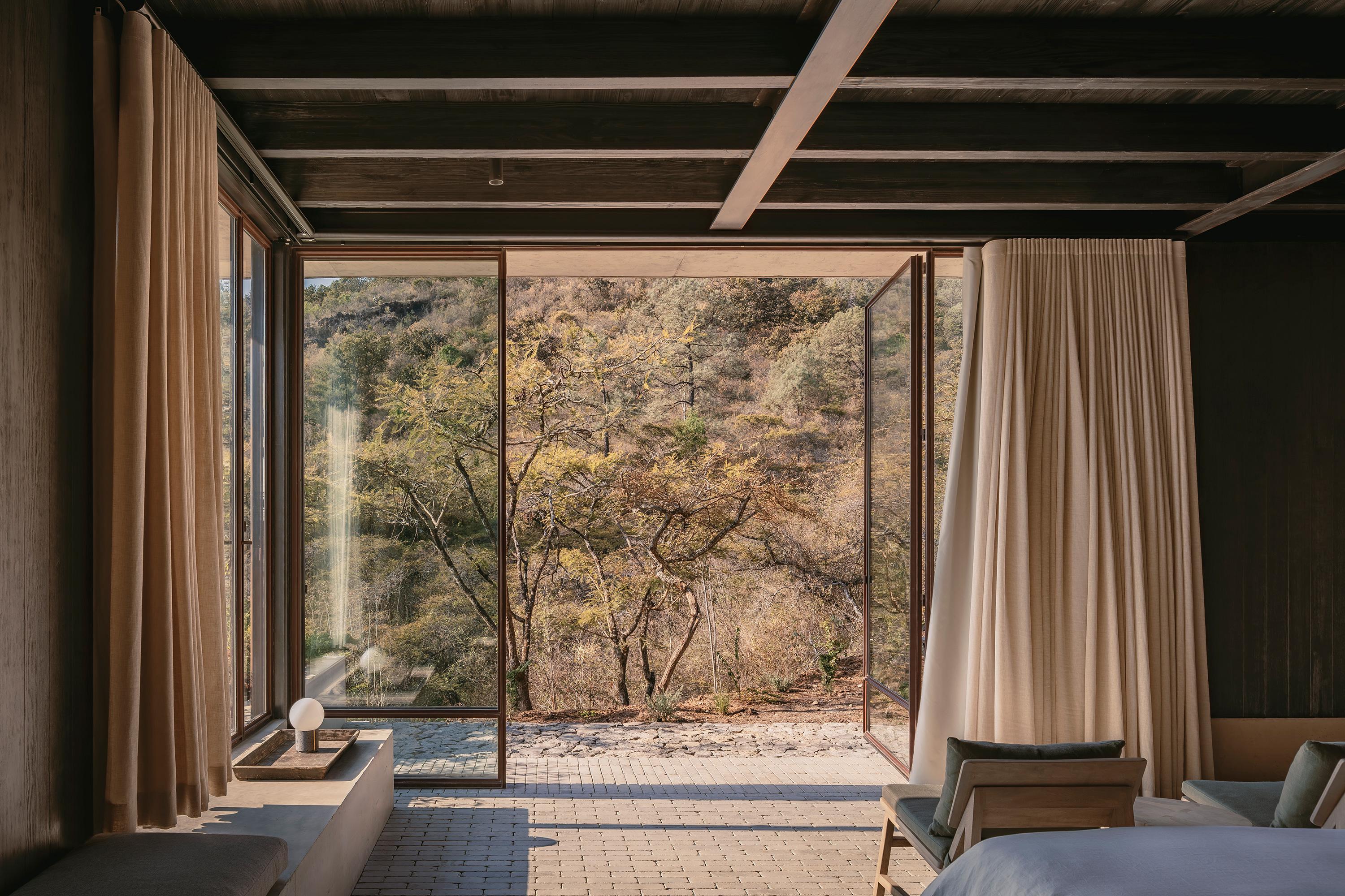Casa el Espino by Soler Orozco Arquitectos — A bedroom interior opens entirely to forest landscape through flush-glazed sliding doors, creating an unobstructed visual threshold.