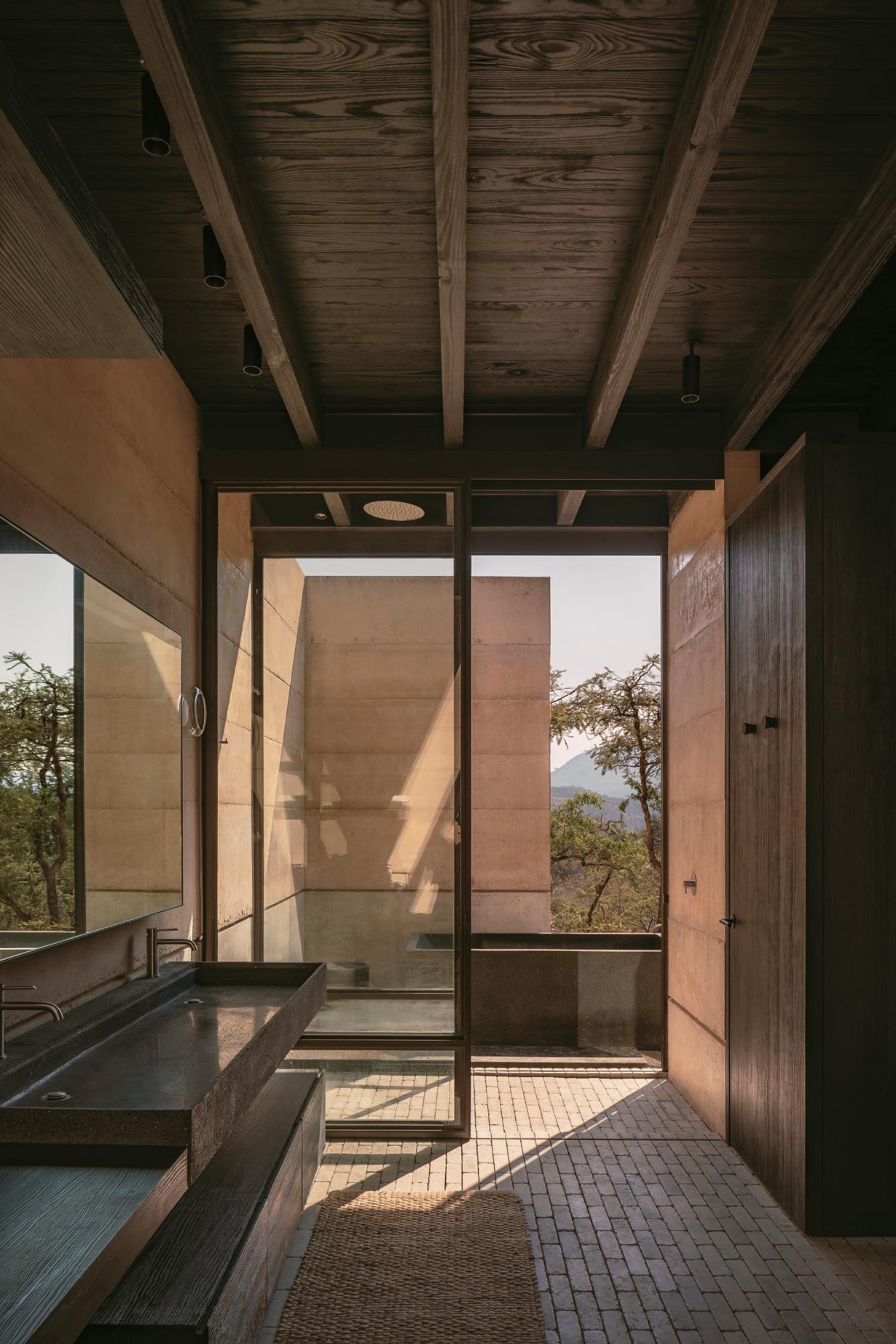 Casa el Espino by Soler Orozco Arquitectos — A bathroom passage frames the landscape through flush-glazed doors with minimal metal framing.