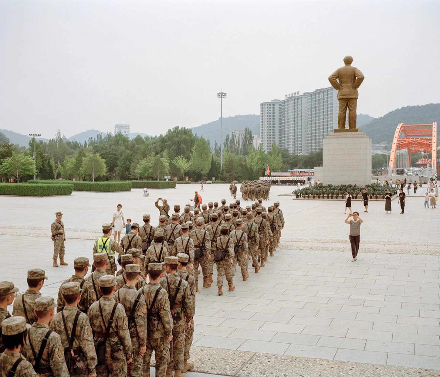 The Internal Crusade by Zexuan Zeng — A bronze statue of a revolutionary figure in military coat stands elevated on a concrete plinth, dominating a vast paved plaza.