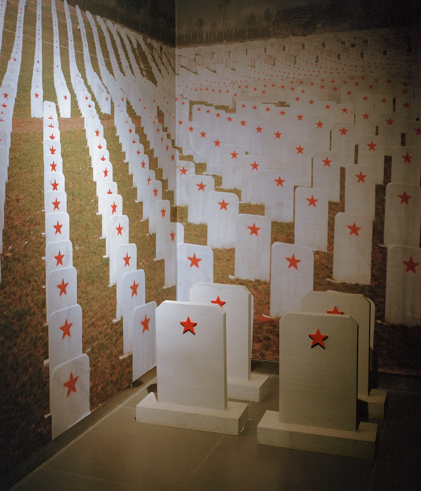 The Internal Crusade by Zexuan Zeng — White paper markers bearing red stars are arranged in dense, receding rows across a gallery floor, creating a grid-like memorial installation.