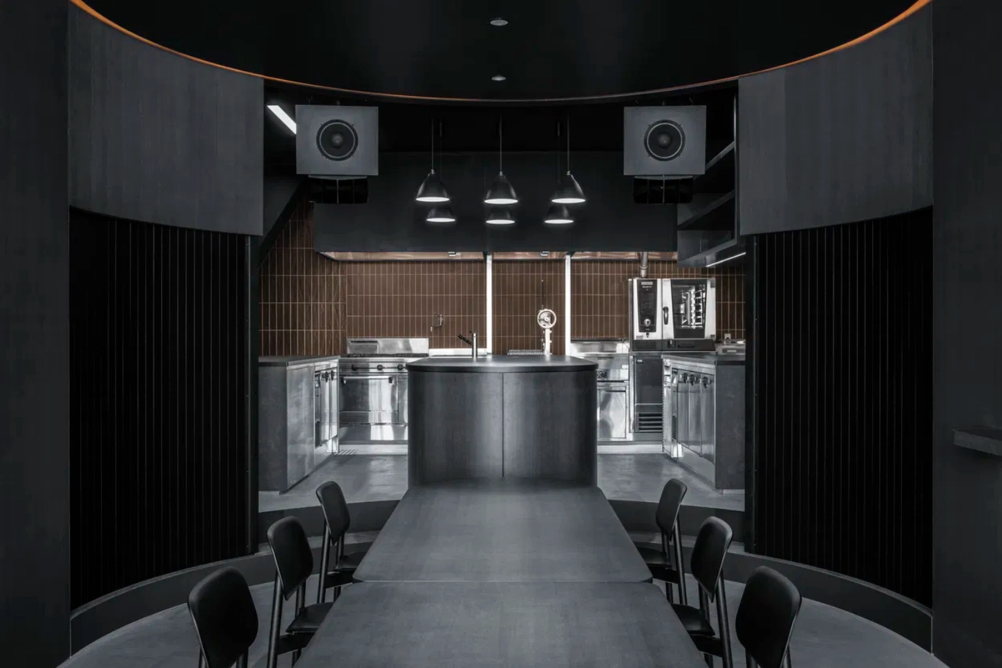 Burnside by Snøhetta — The kitchen viewed from the dining threshold reveals a symmetrical composition anchored by a central stainless steel island.