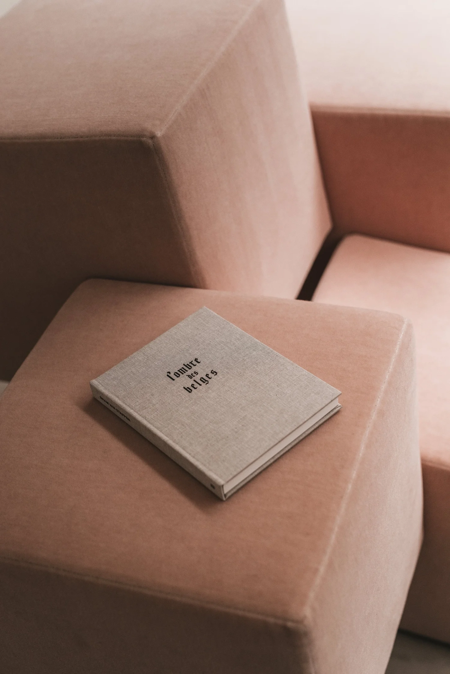 Cubist Chair by ÆTHER/MASS — A single upholstered cubic chair in cream linen occupies the foreground, its soft geometric form resting on an exposed concrete floor with visible aggregate...