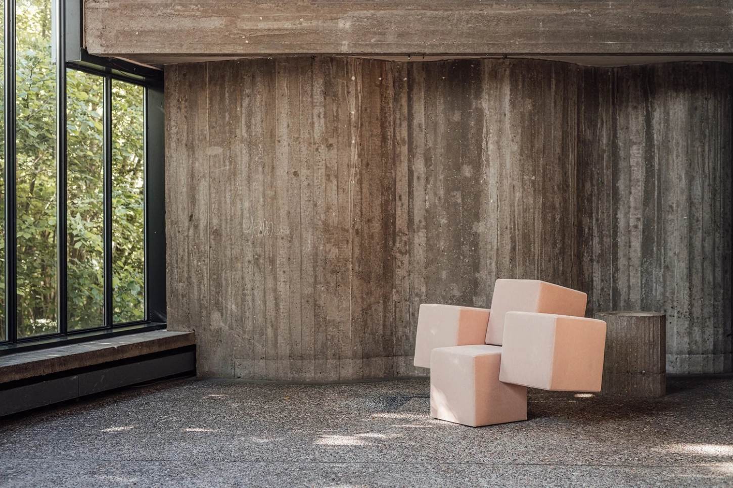 Cubist Chair by ÆTHER/MASS — Three upholstered cubic chairs with soft-edged geometric planes in terracotta and cream occupy the center of a brutalist concrete interior.