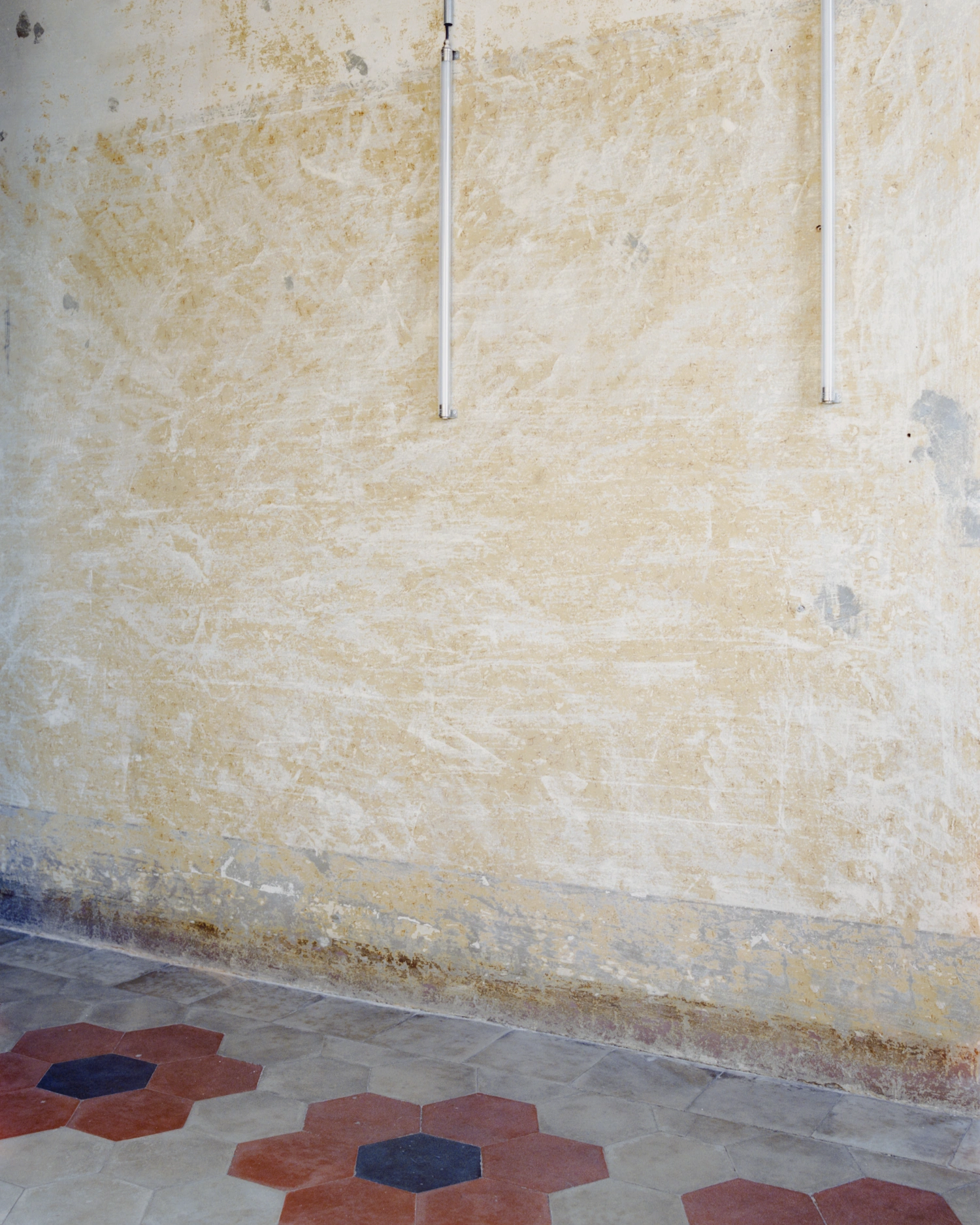 CGM Club Giovanile Milano by co.arch studio — Weathered plaster wall dominates the frame, its cream and off-white surface marked by water stains, efflorescence, and ochre patina that documents years of...