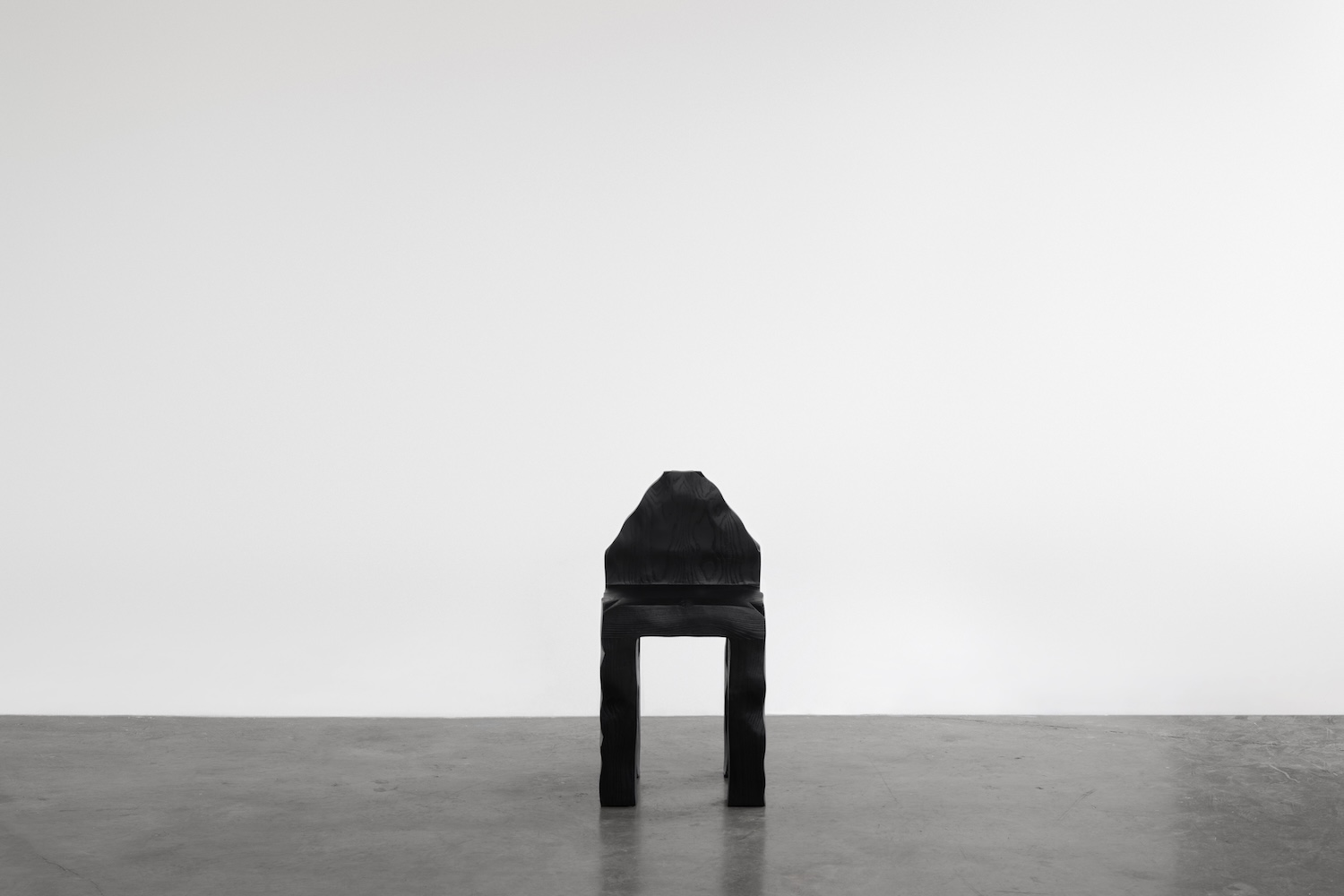 KAMEH 0.5 Collection by KAMEH — A charred timber chair from the KAMEH 0.5 collection sits centered on a concrete floor, its Shou Sugi Ban surface displaying pronounced wood grain...