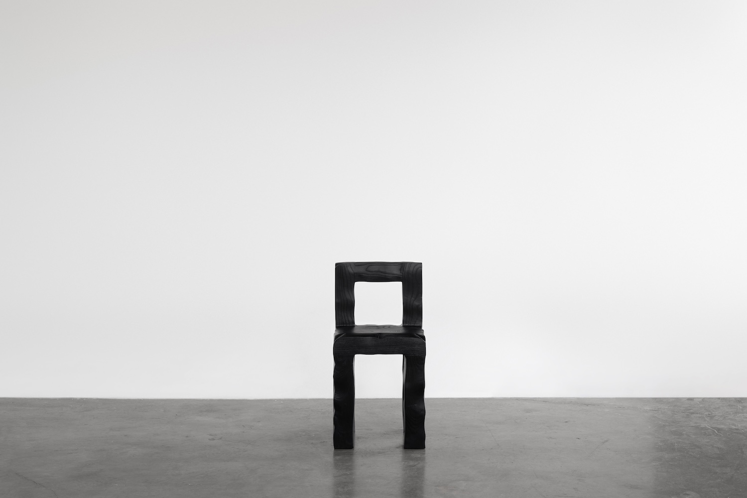 KAMEH 0.5 Collection by KAMEH — A charred timber chair from the KAMEH 0.5 collection sits centered on a concrete floor against a neutral backdrop.
