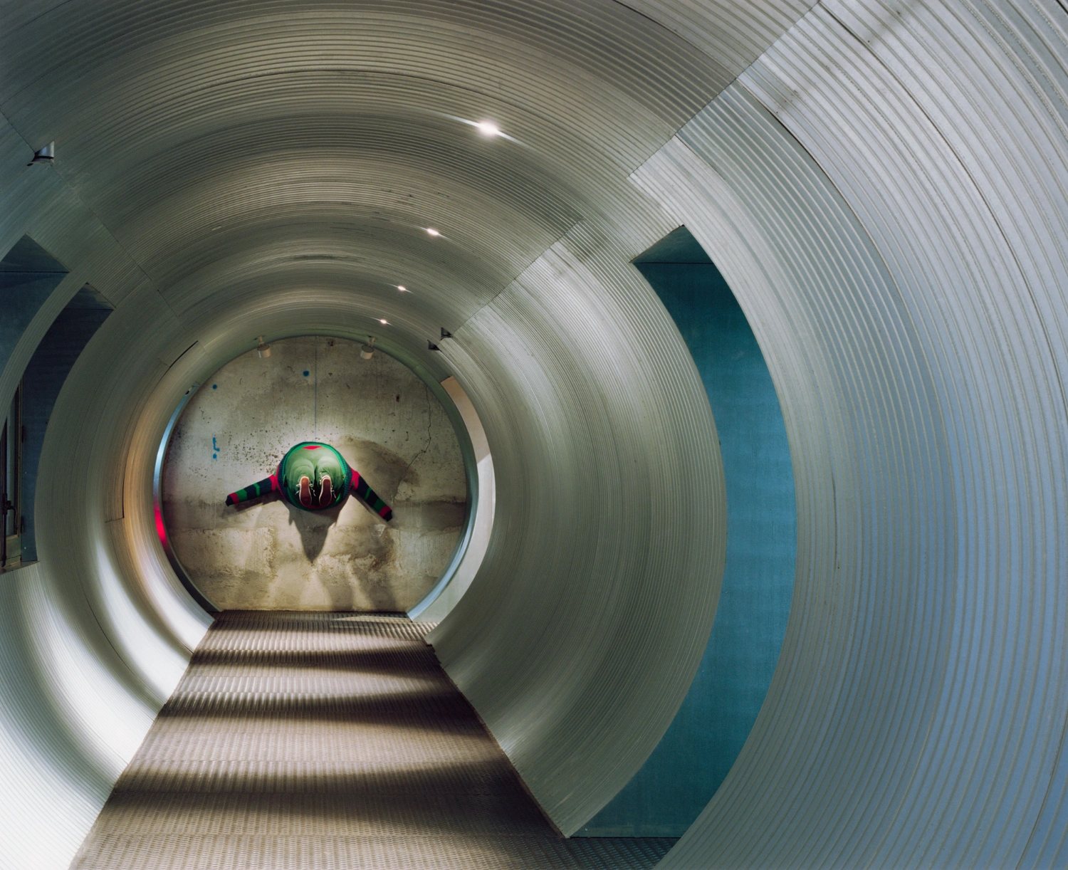SOLO CSV Art Space by Estudio Herreros — A figure in a red and green wingsuit assumes a diving posture within Solo CSV's primary circular aperture, framed by the monolithic concrete ring.