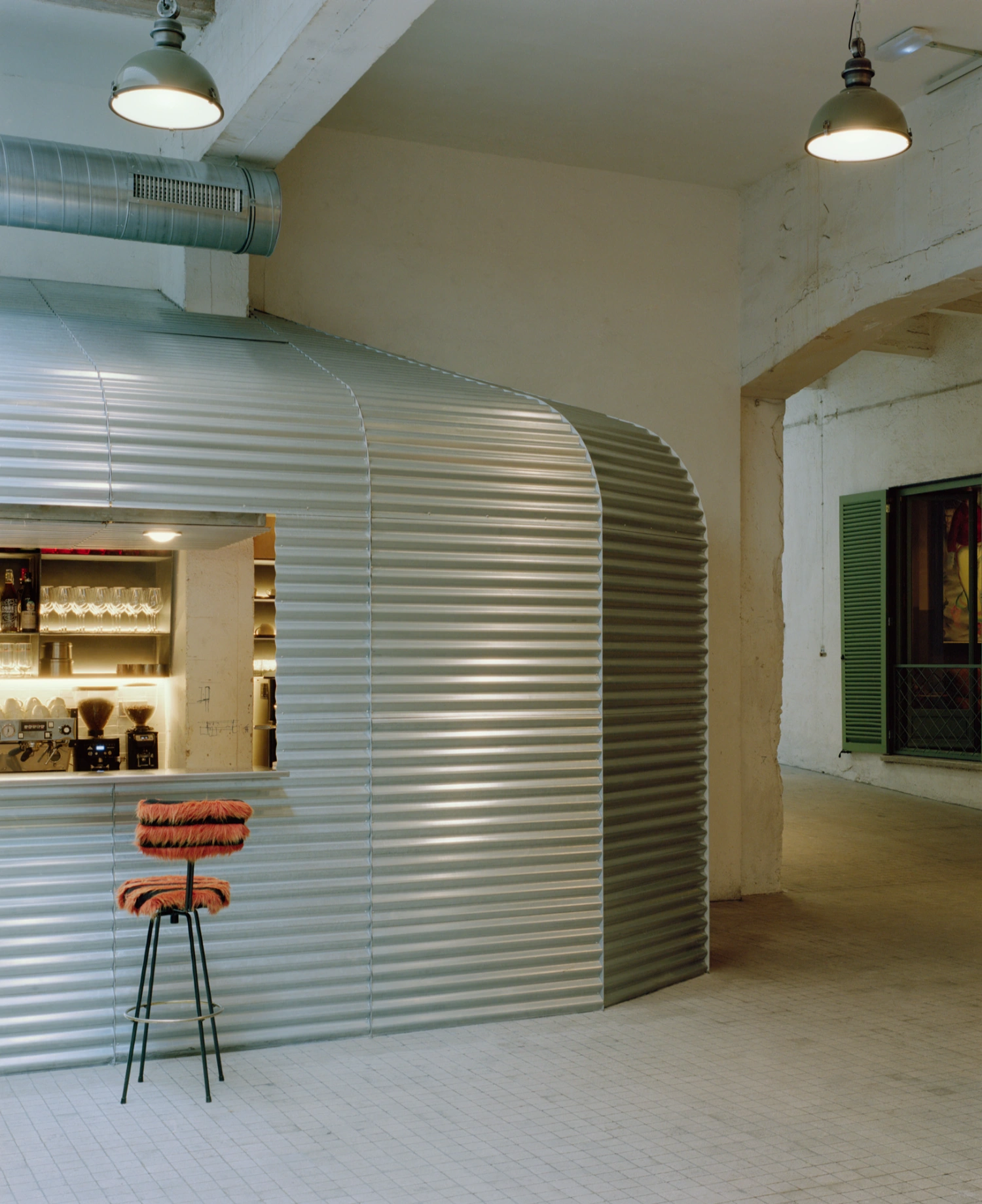 SOLO CSV Art Space by Estudio Herreros — A corrugated metal partition curves through the gallery volume, its horizontal striations catching pendant light in alternating bands of reflection and shadow.