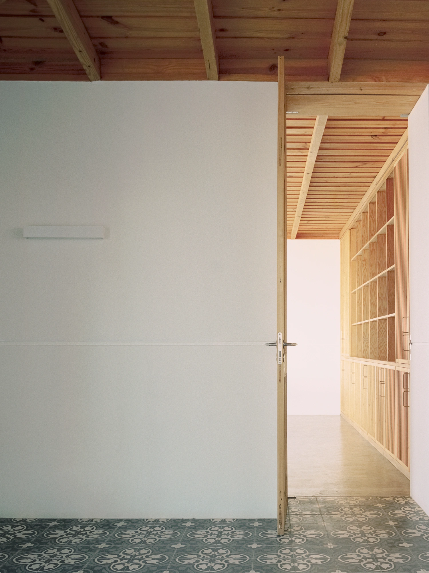 Herdade da Cardeira Winery by EMBAIXADA by EMBAIXADA arquitectura — A passage interior framed through an open wooden door with horizontal slat detailing.