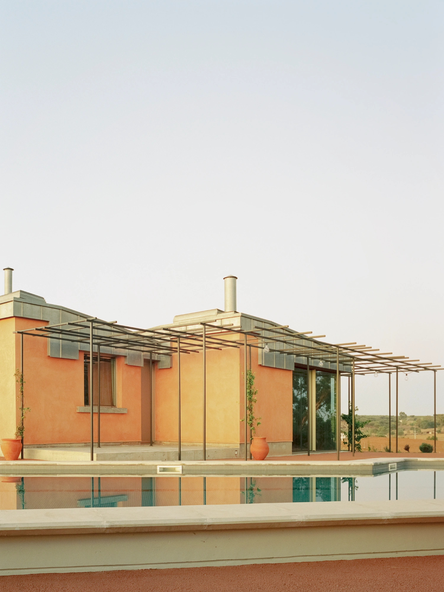 Herdade da Cardeira Winery by EMBAIXADA by EMBAIXADA arquitectura — The poolside elevation reveals EMBAIXADA's material restraint: terracotta render walls meet horizontal bands of patinated metal cladding, their oxidized...