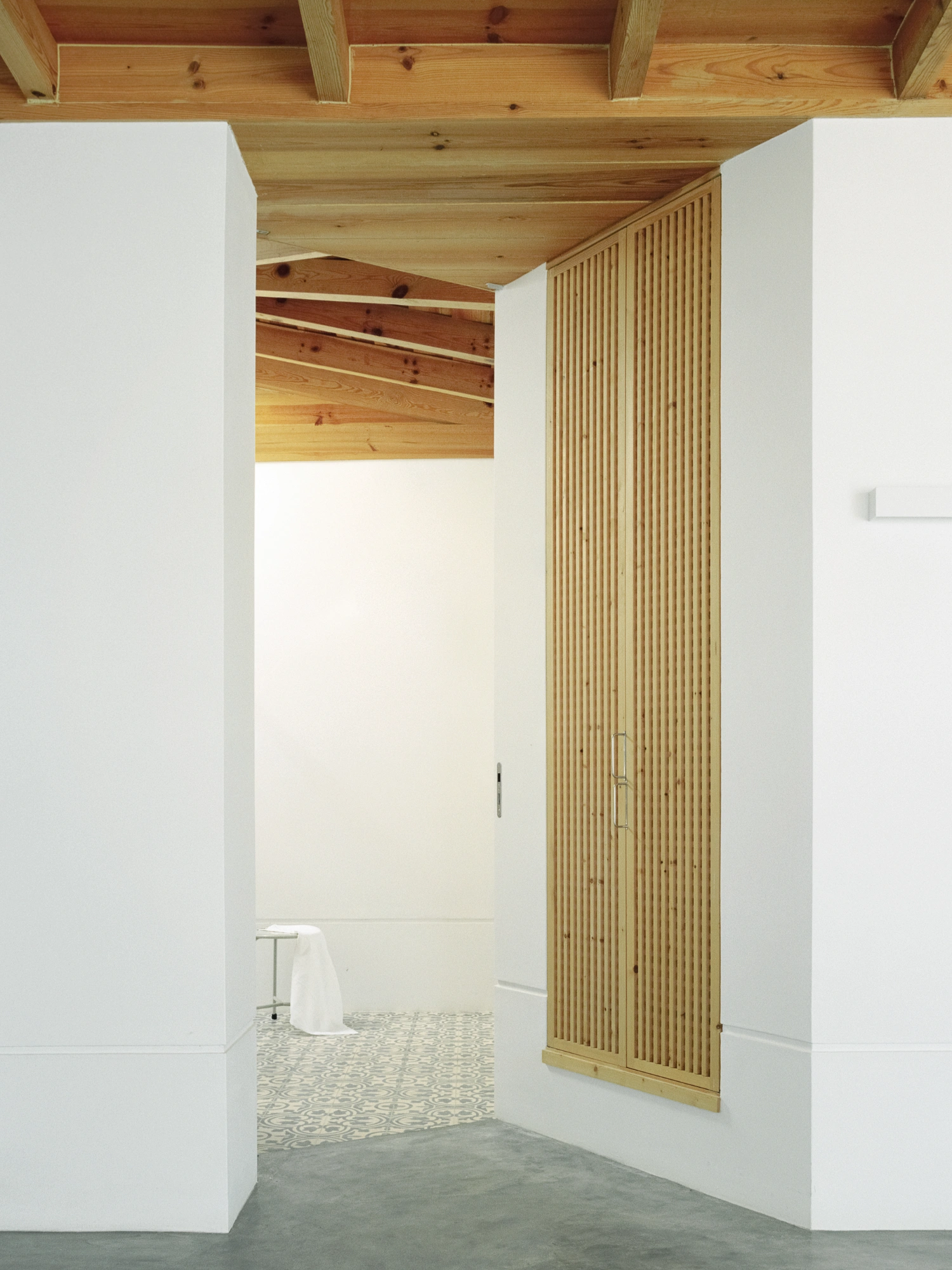 Herdade da Cardeira Winery by EMBAIXADA by EMBAIXADA arquitectura — A timber-lined corridor with vertical pine board cladding forms a narrow passage, framed by white rendered walls on either side.