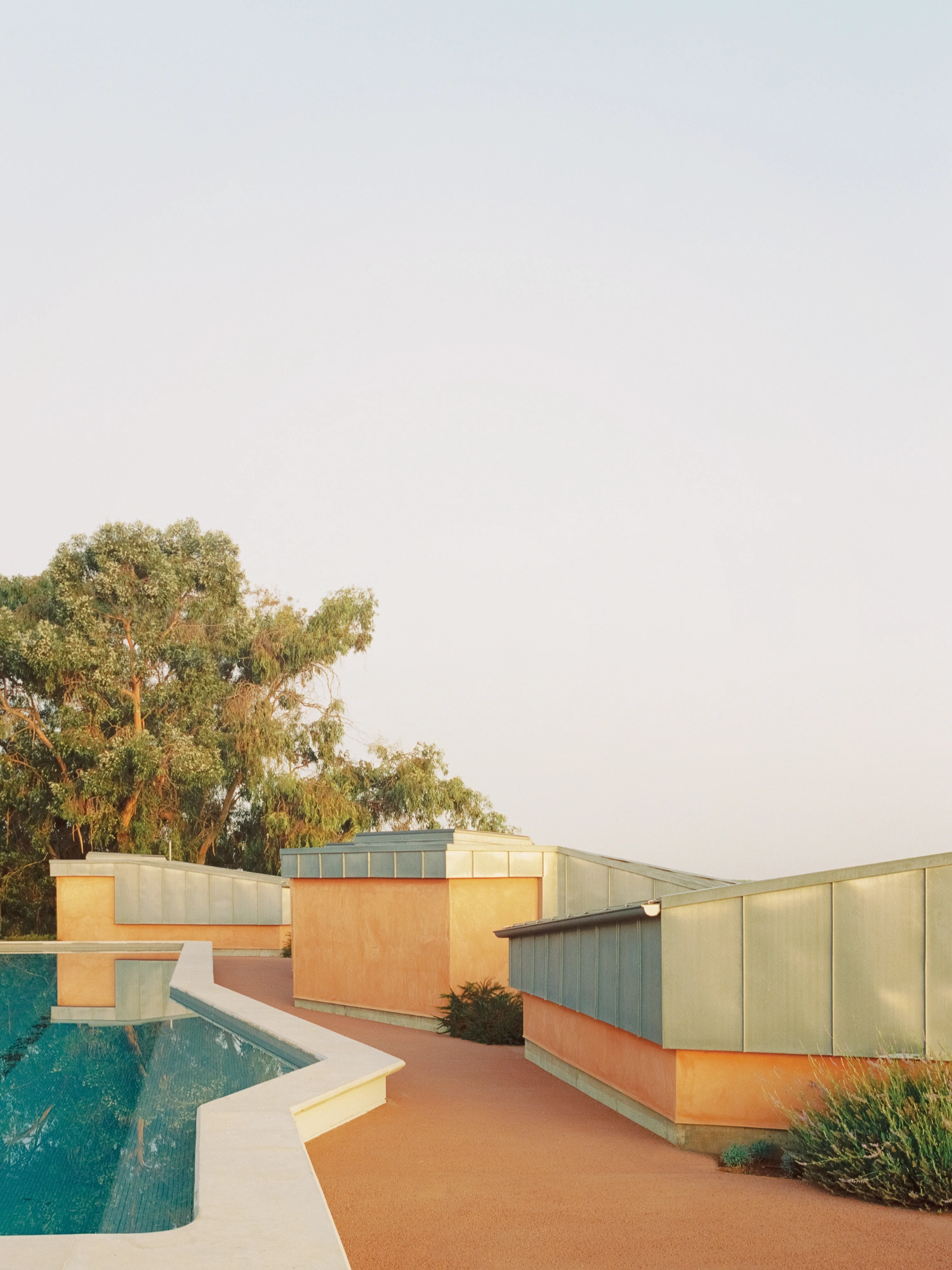 Herdade da Cardeira Winery by EMBAIXADA by EMBAIXADA arquitectura — The winery's terracotta-rendered walls meet oxidized metal cladding in distinct horizontal bands, their weathered patina catching afternoon light.