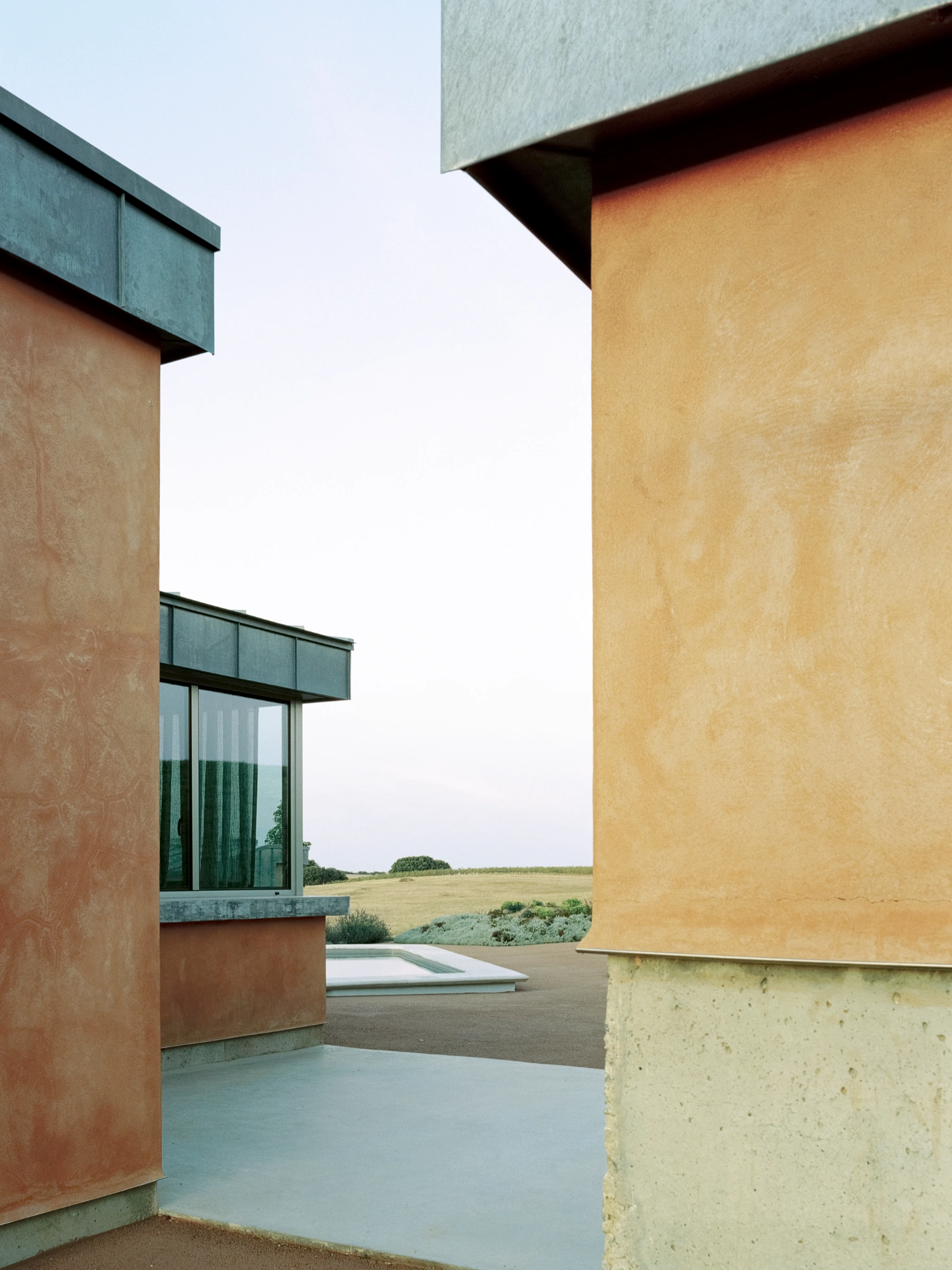 Herdade da Cardeira Winery by EMBAIXADA by EMBAIXADA arquitectura — The photograph frames a narrow passage between two rendered walls in contrasting palettes—terracotta on the left, pale yellow on the right—their surfaces...
