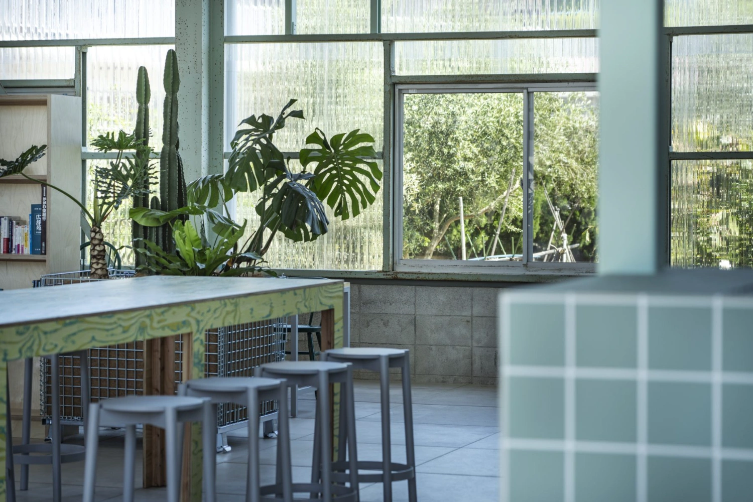 Teshima Factory Cafe by Schemata Architects — The cafeteria interior is framed through translucent corrugated polycarbonate panels, creating a greenhouse-like enclosure with pronounced linear shadow...