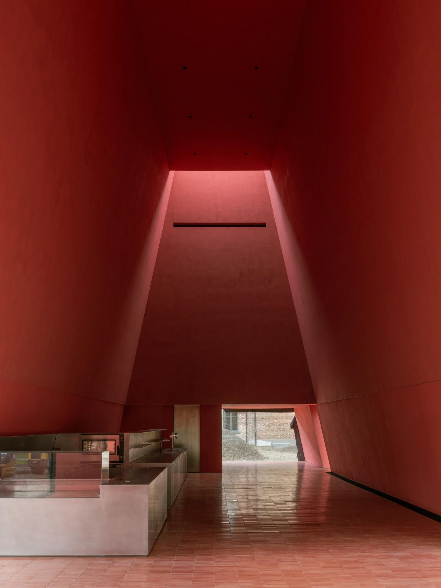 Abby Kortrijk by BAROZZI VEIGA — A monolithic red-brick interior volume tapers upward toward a skylight aperture, creating a trapezoidal void within the Abbey Kortrijk renovation.