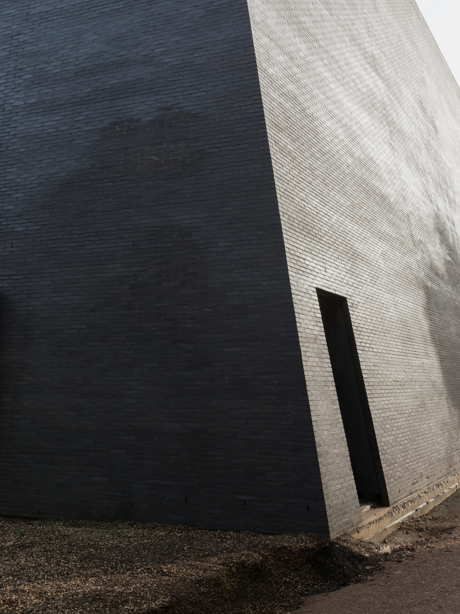 Abby Kortrijk by BAROZZI VEIGA — A trapezoidal black brick tower rises sharply against the light-colored brick of the adjacent heritage structure.