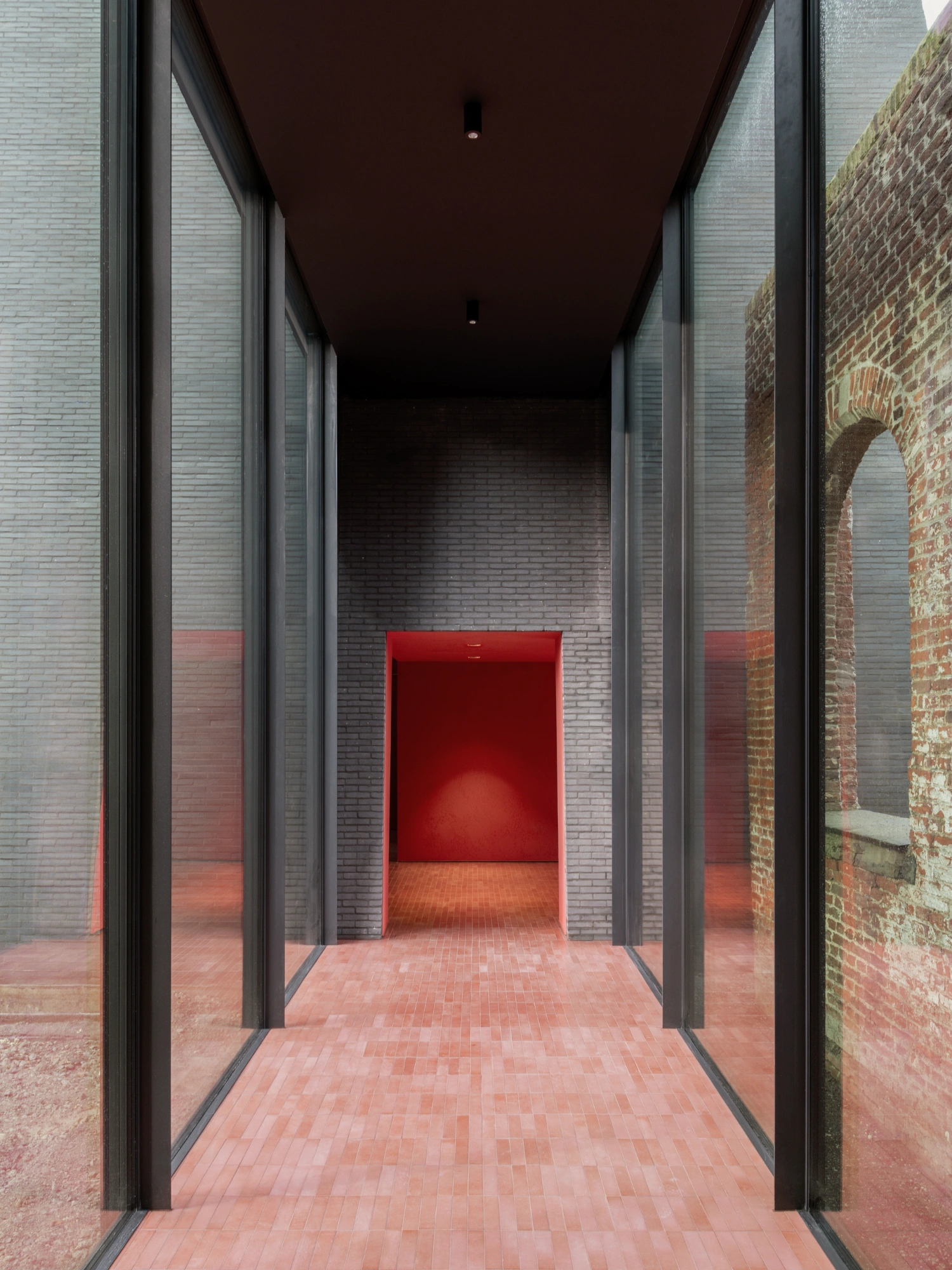 Abby Kortrijk by BAROZZI VEIGA — A symmetrical corridor passage frames a recessed red interior volume at the abbey's threshold.