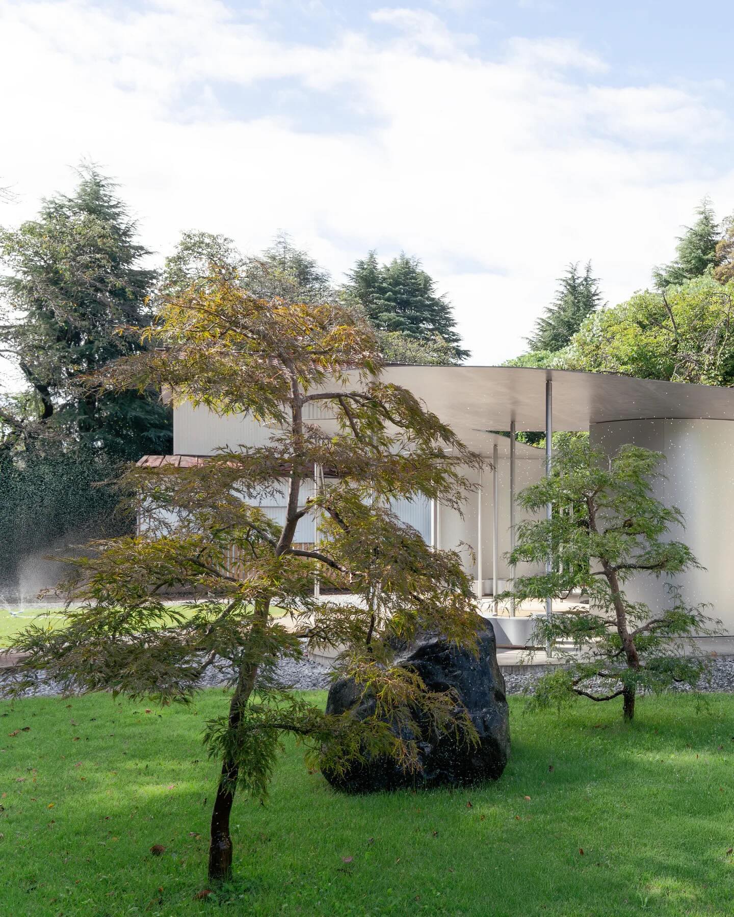 Sonei-ji Cemetery Pavilion (Muyujurin) by SANAA — A Japanese garden scene frames the Sonei-ji Cemetery Pavilion through layered vegetation.