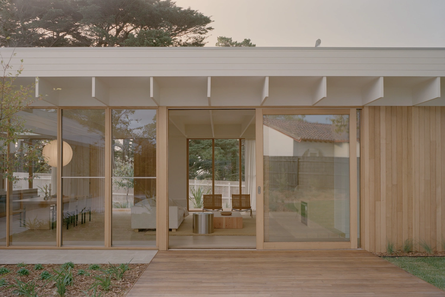 Mount Martha House by Victoria Merrett Architects — The rear facade presents a continuous glazed wall system with timber-framed mullions spanning the full width, punctuated by regularly spaced white concrete...