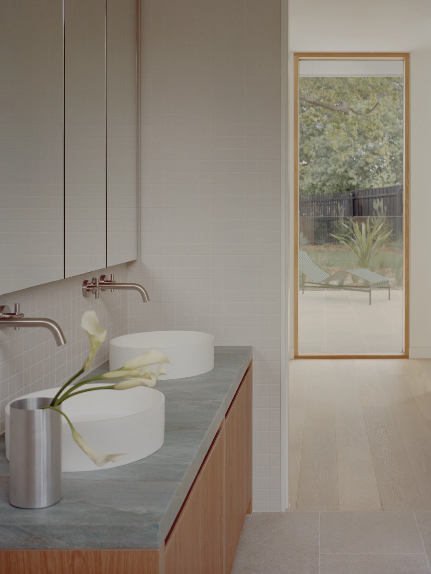 Mount Martha House by Victoria Merrett Architects — The bathroom extends the residence's material language through a dual-basin configuration mounted on a grey stone countertop with warm timber cabinetry below.