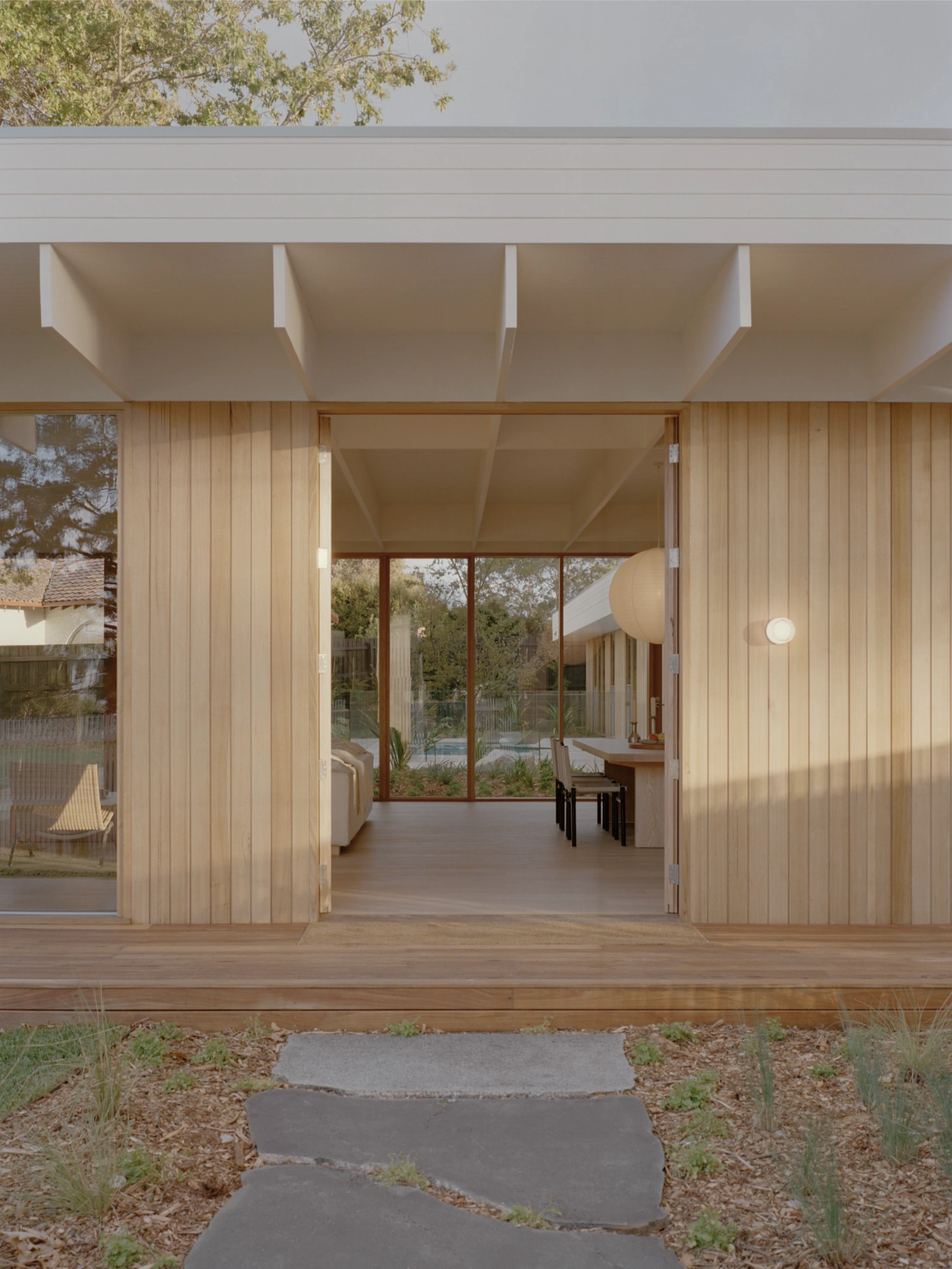 Mount Martha House by Victoria Merrett Architects — The rear facade presents a continuous glazed wall system with timber-framed mullions spanning the full width, framed by vertical timber cladding in warm...