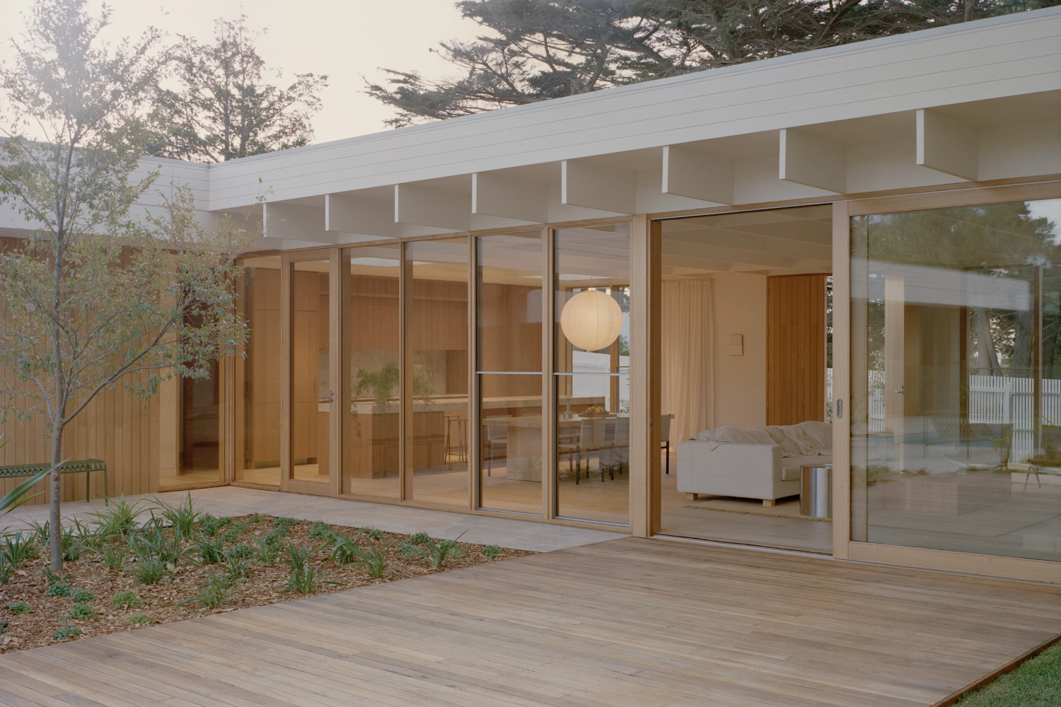 Mount Martha House by Victoria Merrett Architects — The rear façade of Mount Martha House presents a continuous glazed wall system with timber-framed mullions spanning the full width, opening onto a timber...