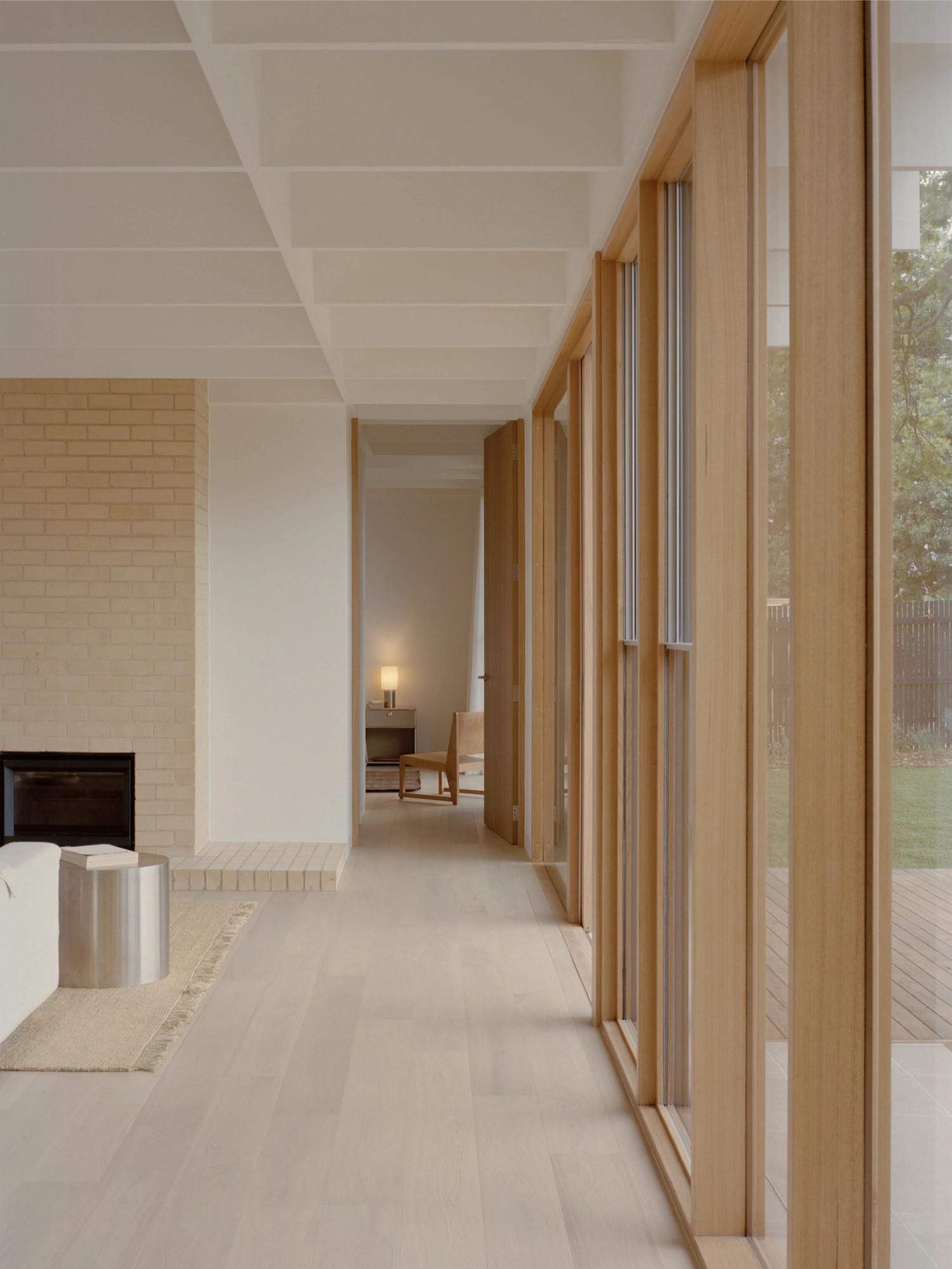Mount Martha House by Victoria Merrett Architects — A glazed corridor frames views toward a secondary bedroom suite, its timber-mullioned fenestration system creating a rhythmic visual grid across the rear...