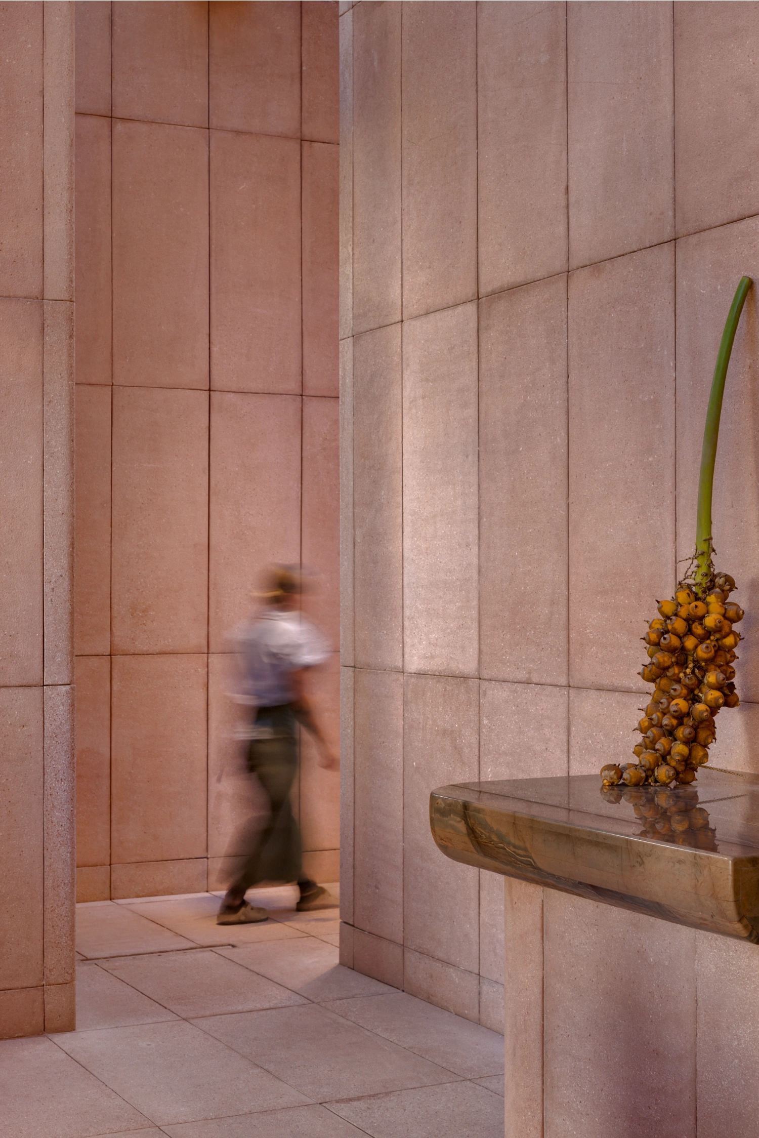 Rubra Restaurant by Ignacio Urquiza + Ana Paula de Alba — A motion-blurred figure traverses a corridor lined with mauve-pink ceramic tiles arranged in a uniform grid pattern, their vertical grout lines creating...