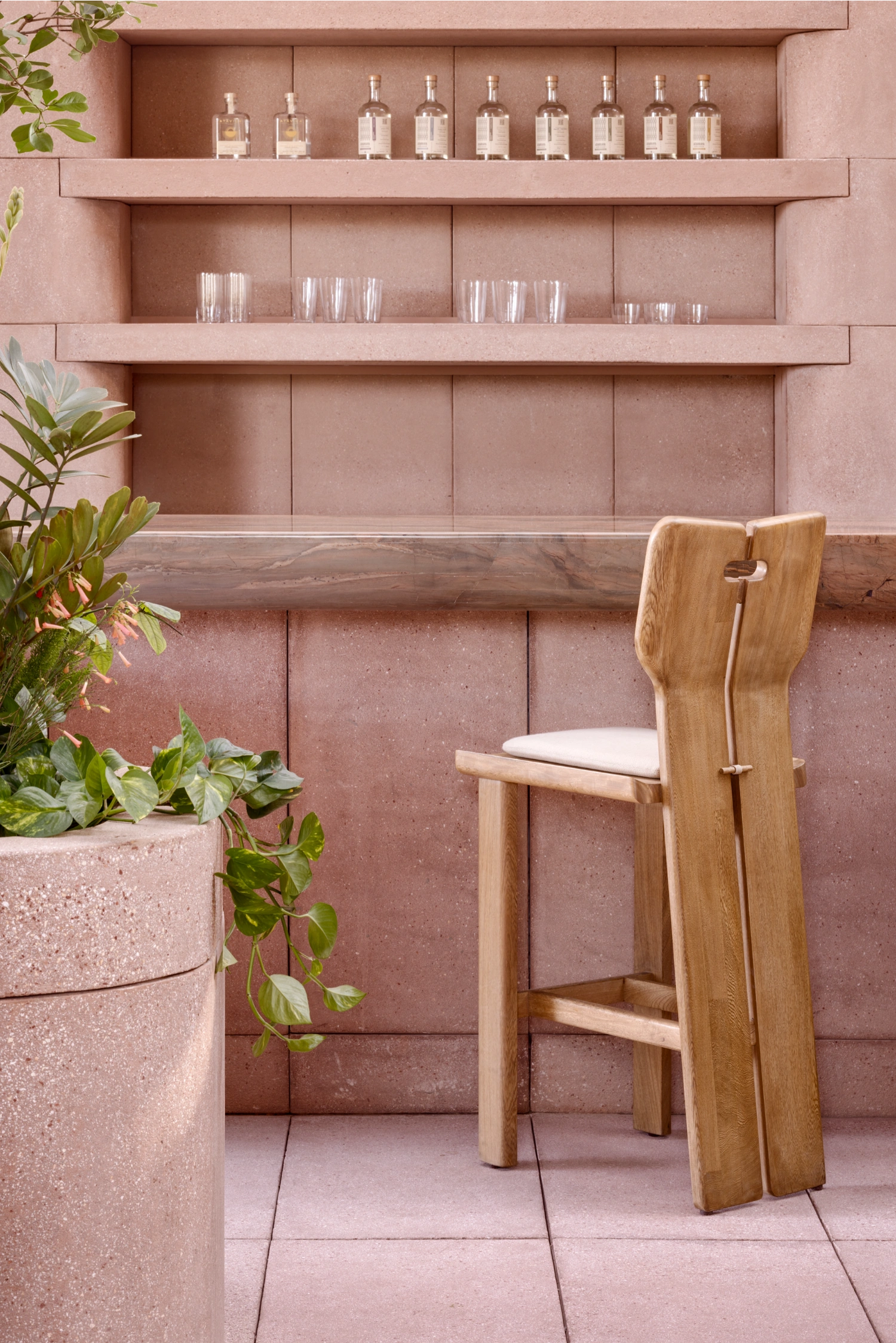 Rubra Restaurant by Ignacio Urquiza + Ana Paula de Alba — A wooden bar stool with curved backrest and cream cushion sits centered before a mauve-pink ceramic tile wall, its vertical grout lines establishing strong...
