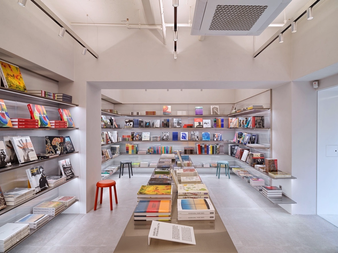 MoMA Bookstore at Hyundai Card in Seoul — The MoMA Bookstore interior reveals a studied retail geometry: floor-to-ceiling white shelving systems organize art books and catalogs across opposing...