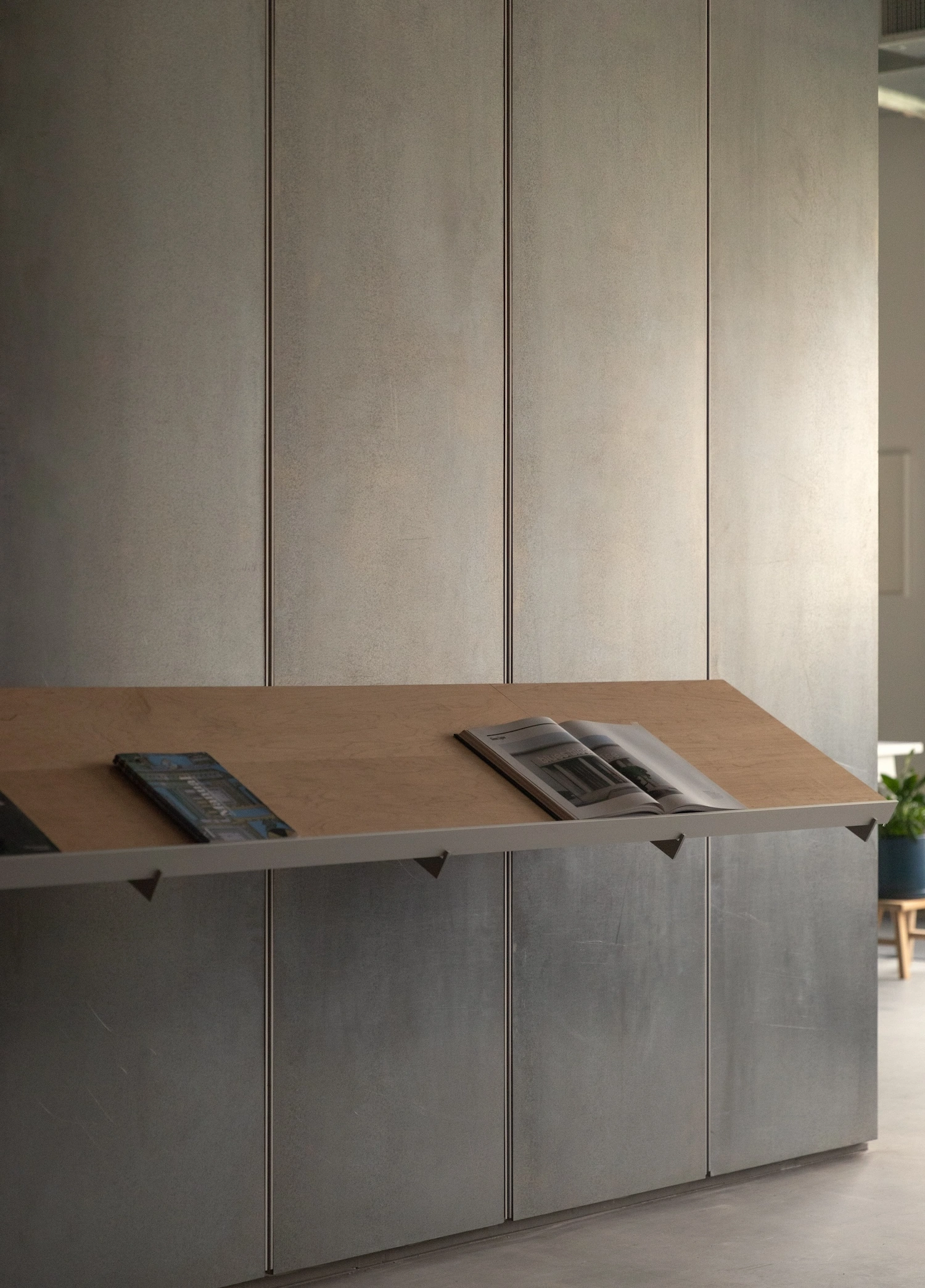 Glenn Ligon Artist’s Studio by Ravi Raj Architect — A horizontal timber shelf with steel cantilever brackets spans across a concrete block wall base, displaying magazines and materials.