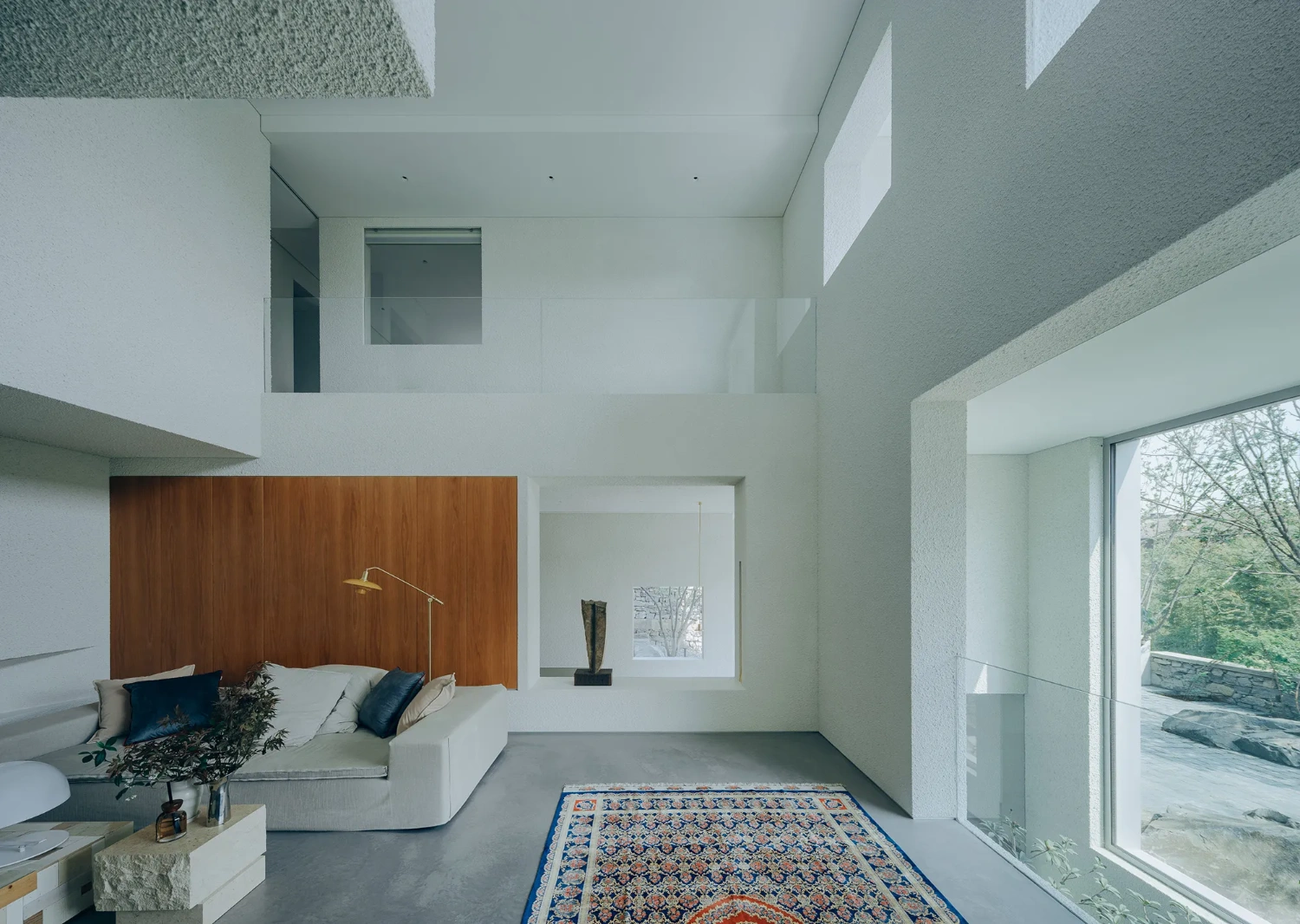 House J in Beijing by Atelier About Architecture — The double-height living space showcases a layered interior composition with a distinctive wooden accent wall in warm walnut tones positioned behind a...