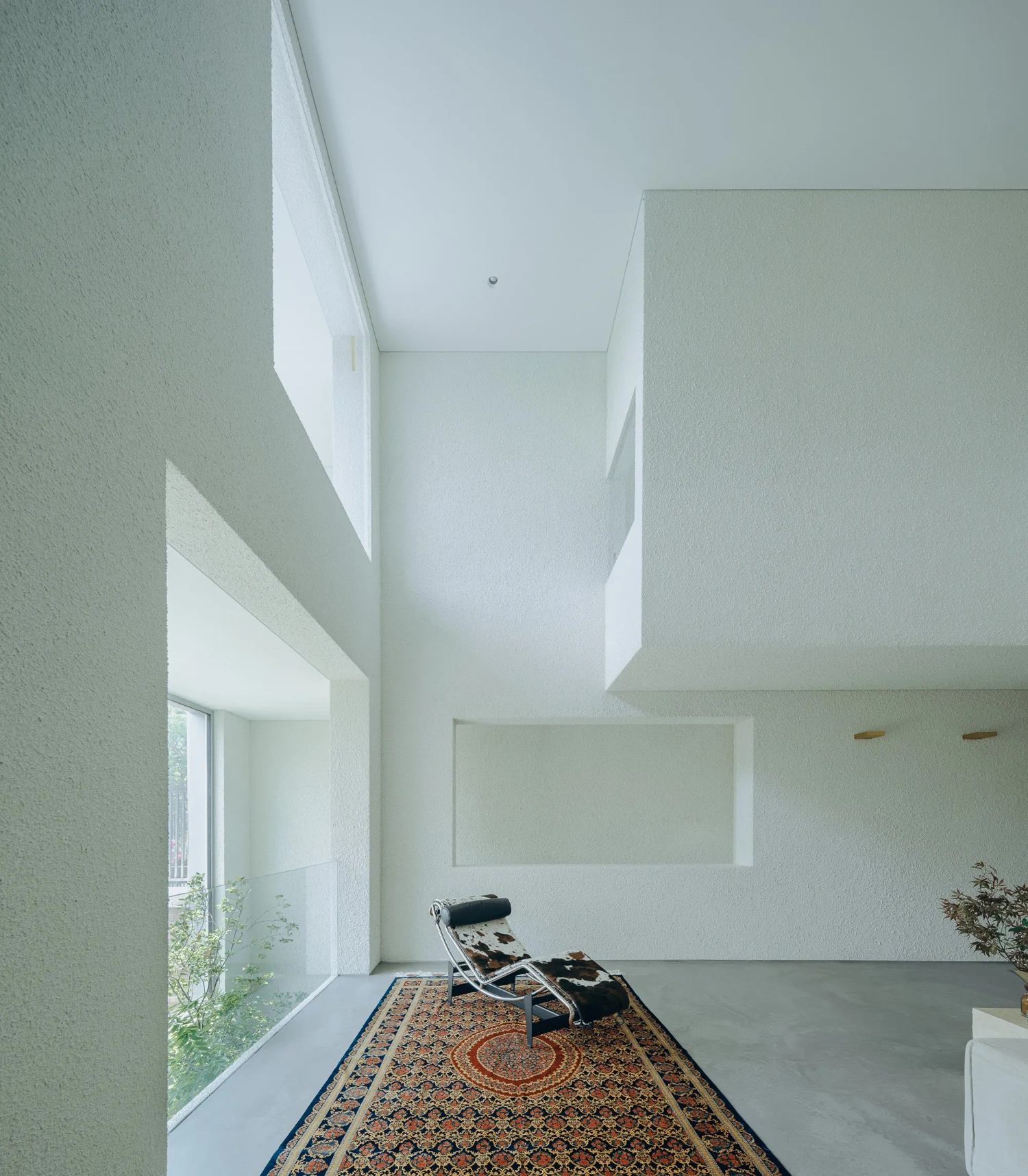 House J in Beijing by Atelier About Architecture — A narrow interior passage frames a black lounge chair positioned on a patterned rug, anchoring an otherwise minimal composition.