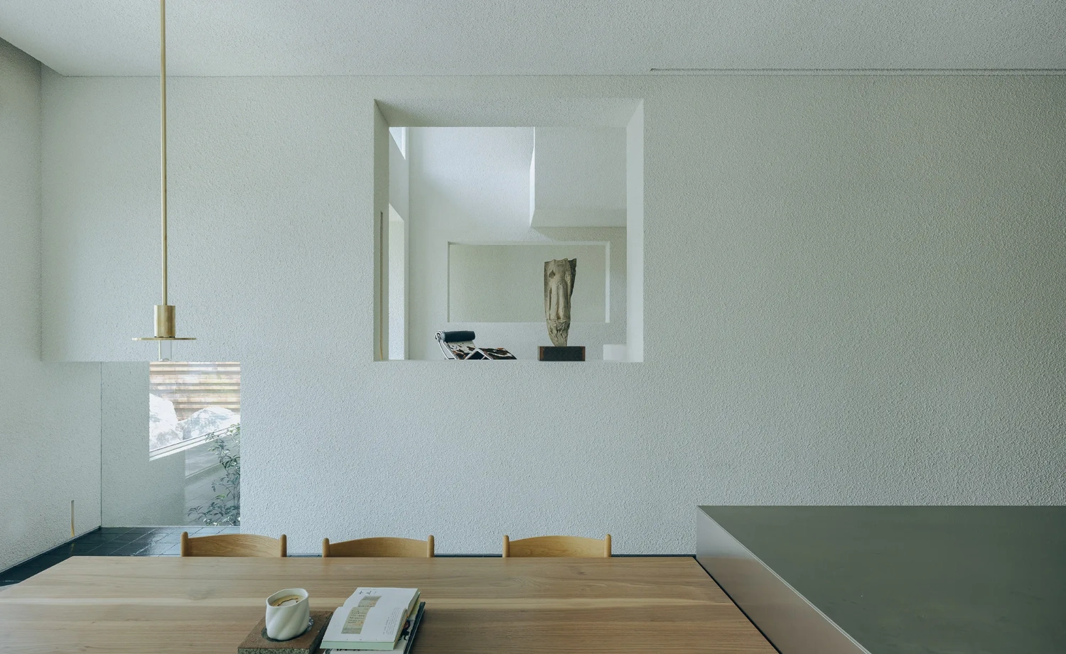 House J in Beijing by Atelier About Architecture — A dining room flooded with overhead skylight that illuminates the wood table and three wishbone chairs arranged asymmetrically across the foreground.