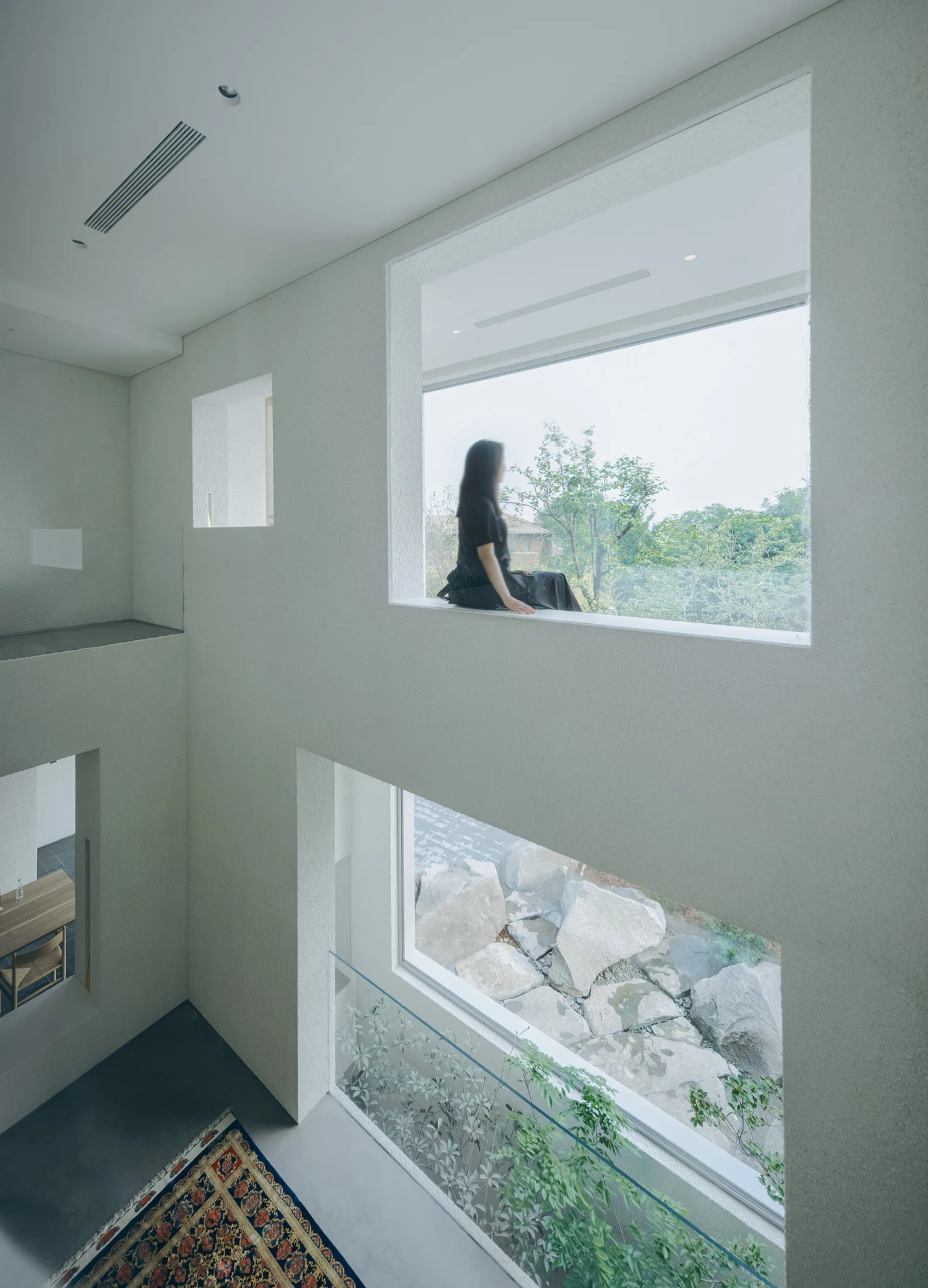 House J in Beijing by Atelier About Architecture — A double-height interior passage frames layered views through two horizontal windows of differing scales.