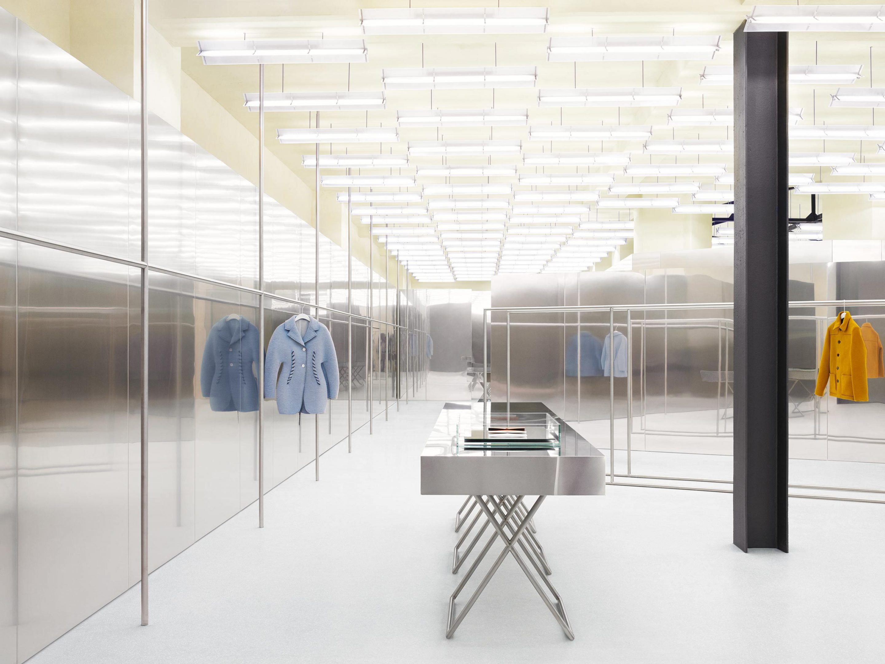 Acne Studios by Bubab Architects — A minimalist retail corridor defined by recessed linear fluorescent strips spanning the pale yellow ceiling in rigid parallel rows, establishing sharp...