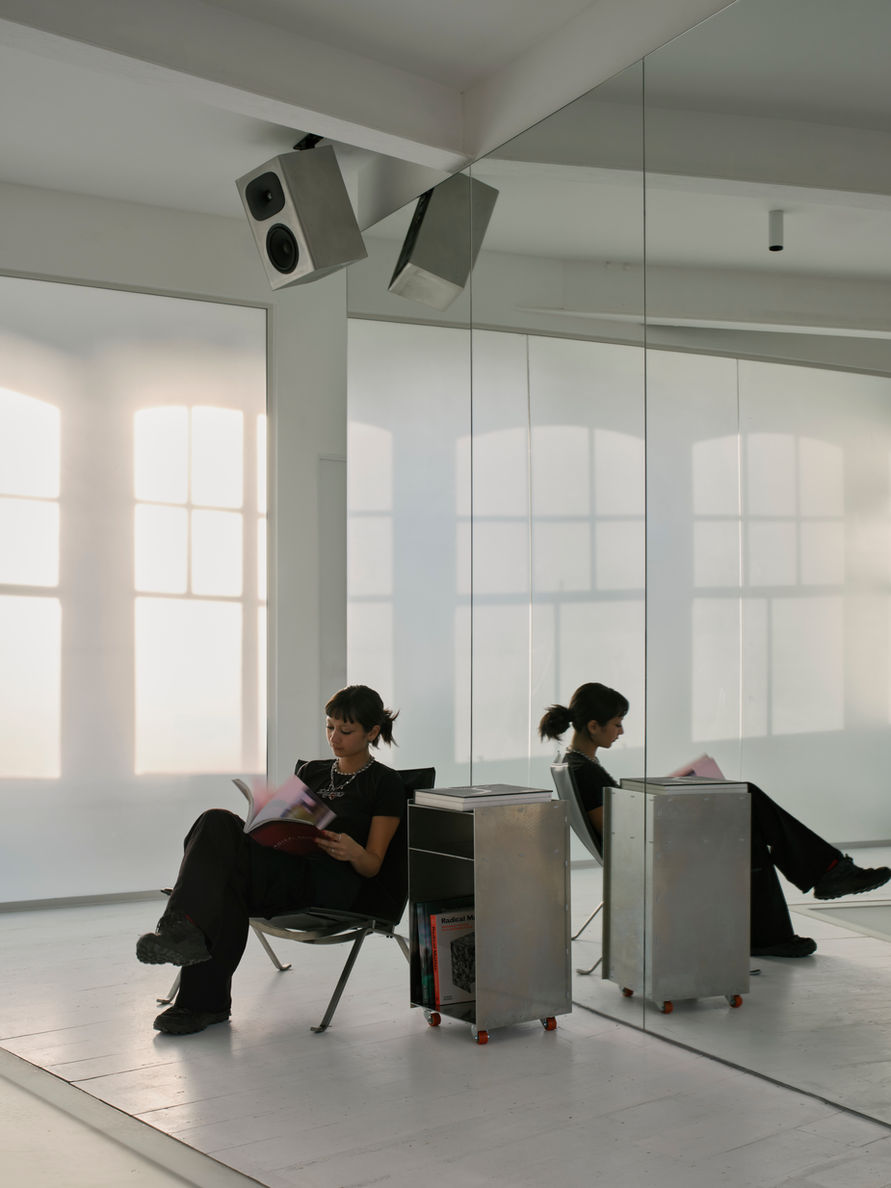 Salt Salon by unknown works — A figure sits reading within a mirrored alcove, creating a doubled reflection against large-format ceramic tiles laid horizontally.